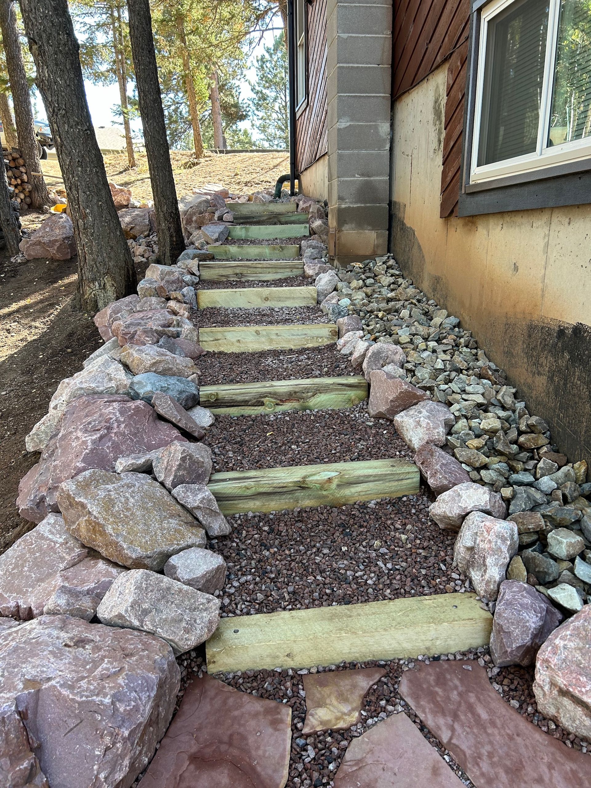 A stone walkway leading to a house with wooden steps and rocks.