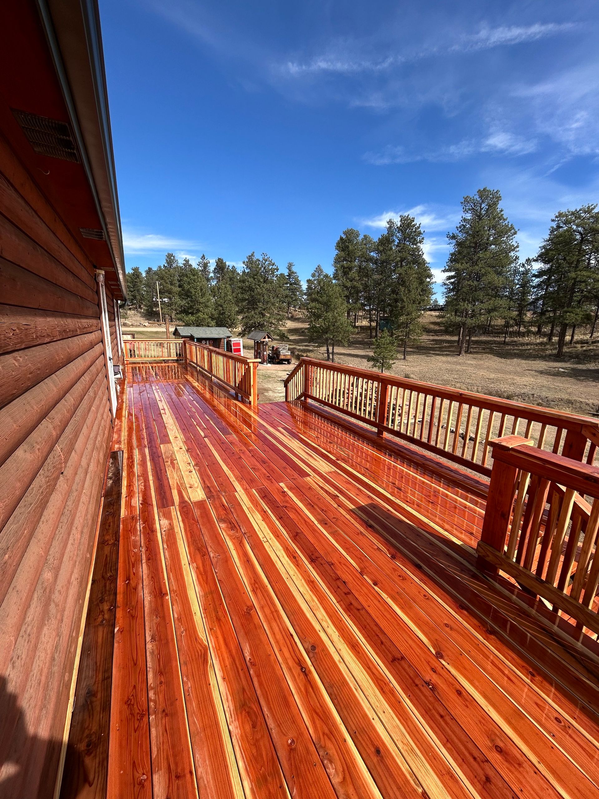 A large wooden deck with a railing and trees in the background.