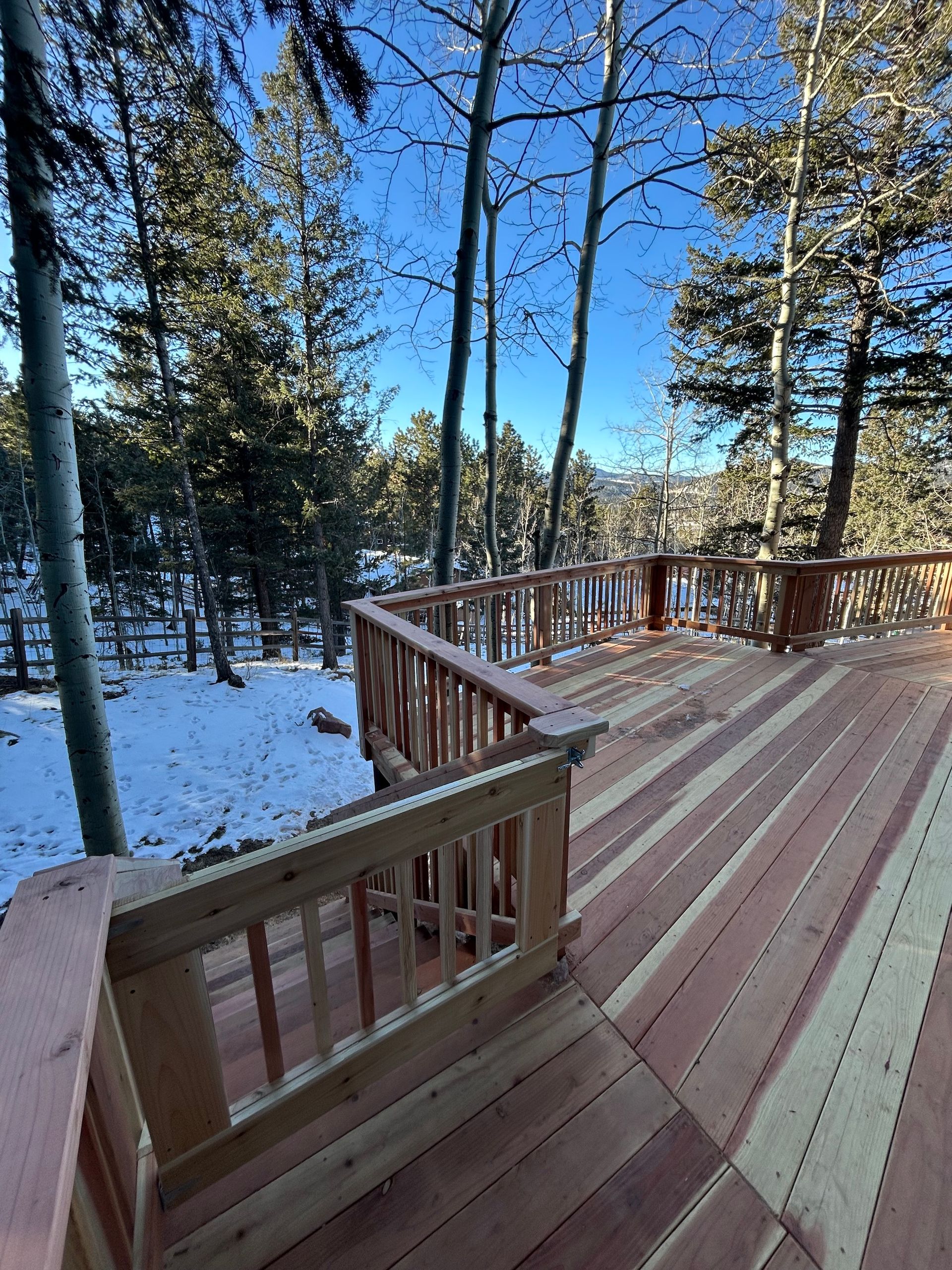 A wooden deck with a railing overlooking a snowy forest.