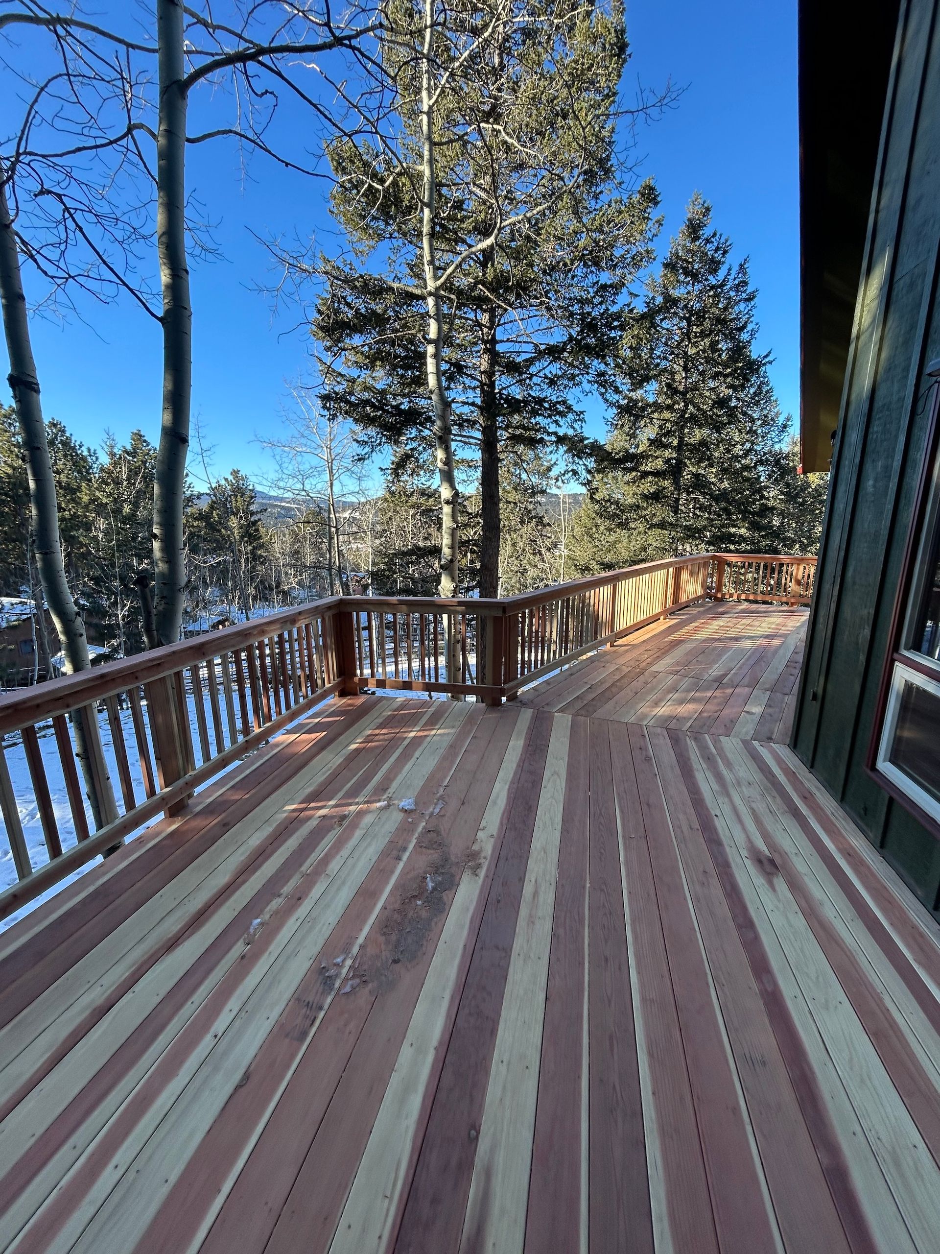 A large wooden deck with a railing and trees in the background.