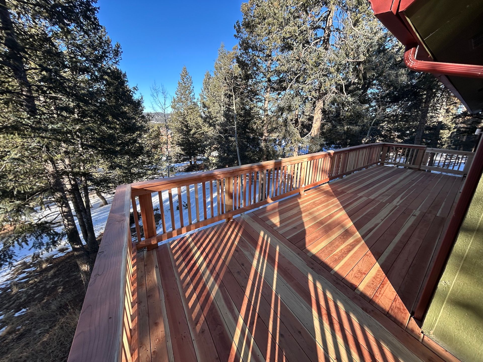 A large wooden deck with a railing and trees in the background.