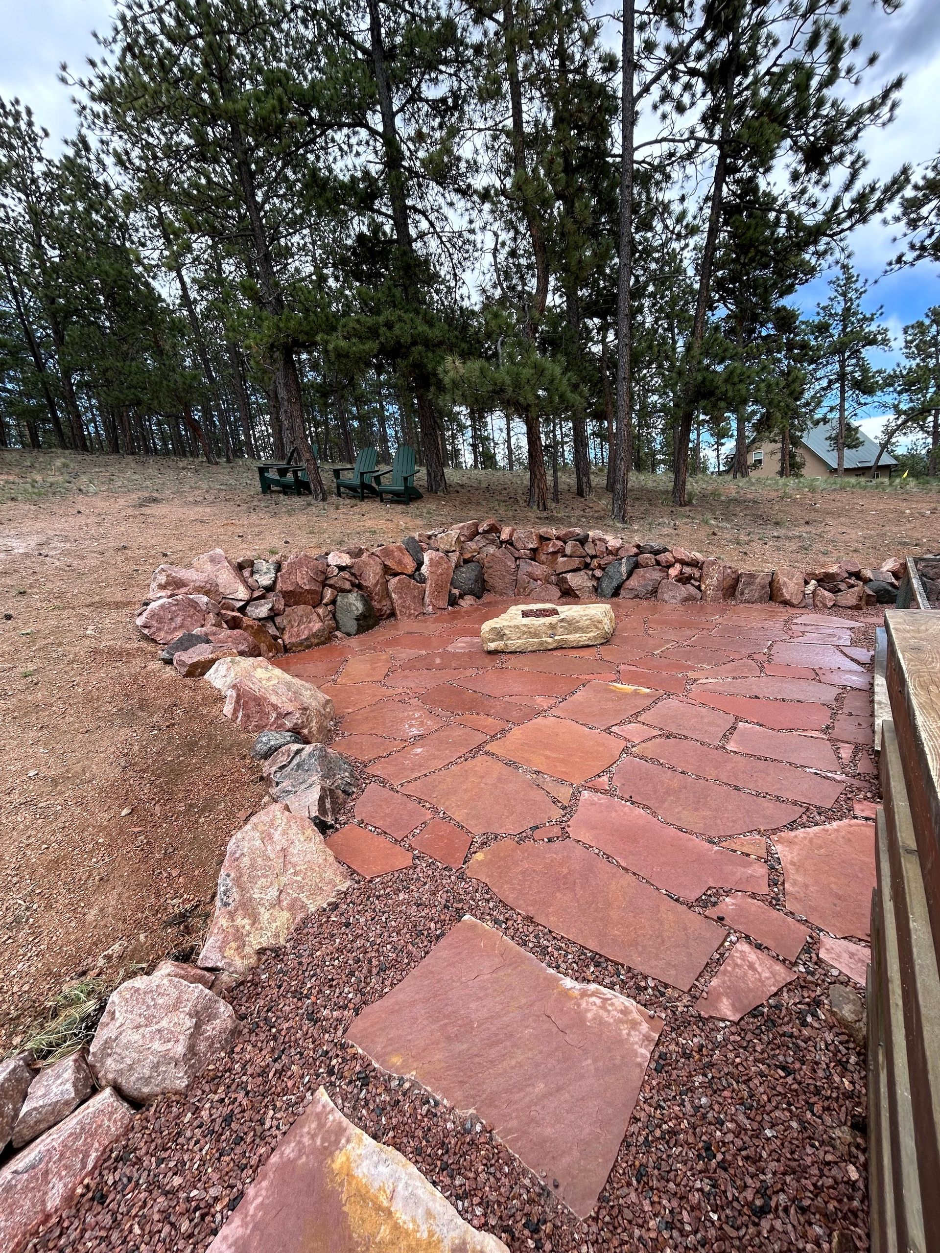 A stone walkway leading to a fire pit in the middle of a field with trees in the background.