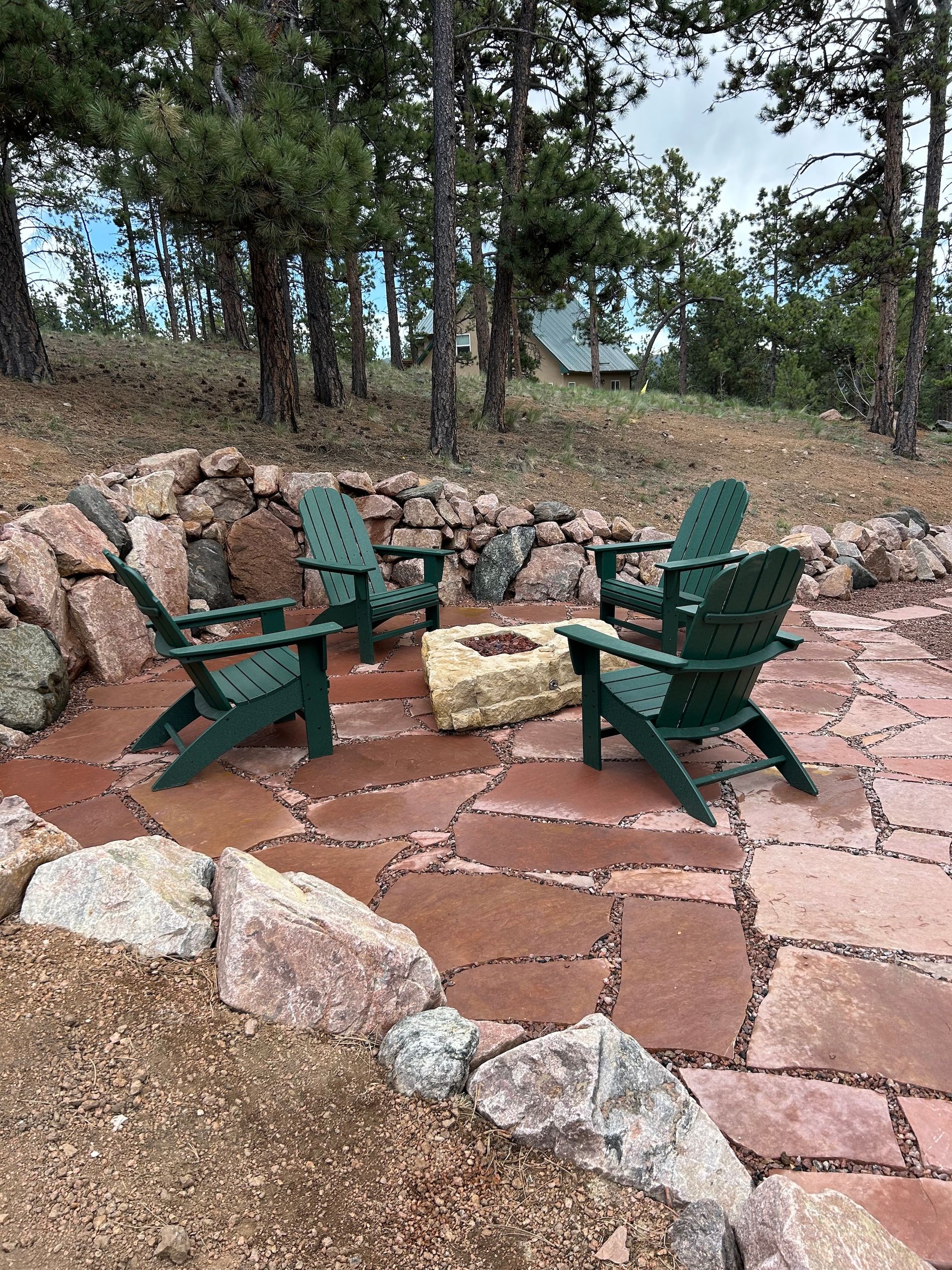 Two green chairs are sitting on a stone patio next to a fire pit.