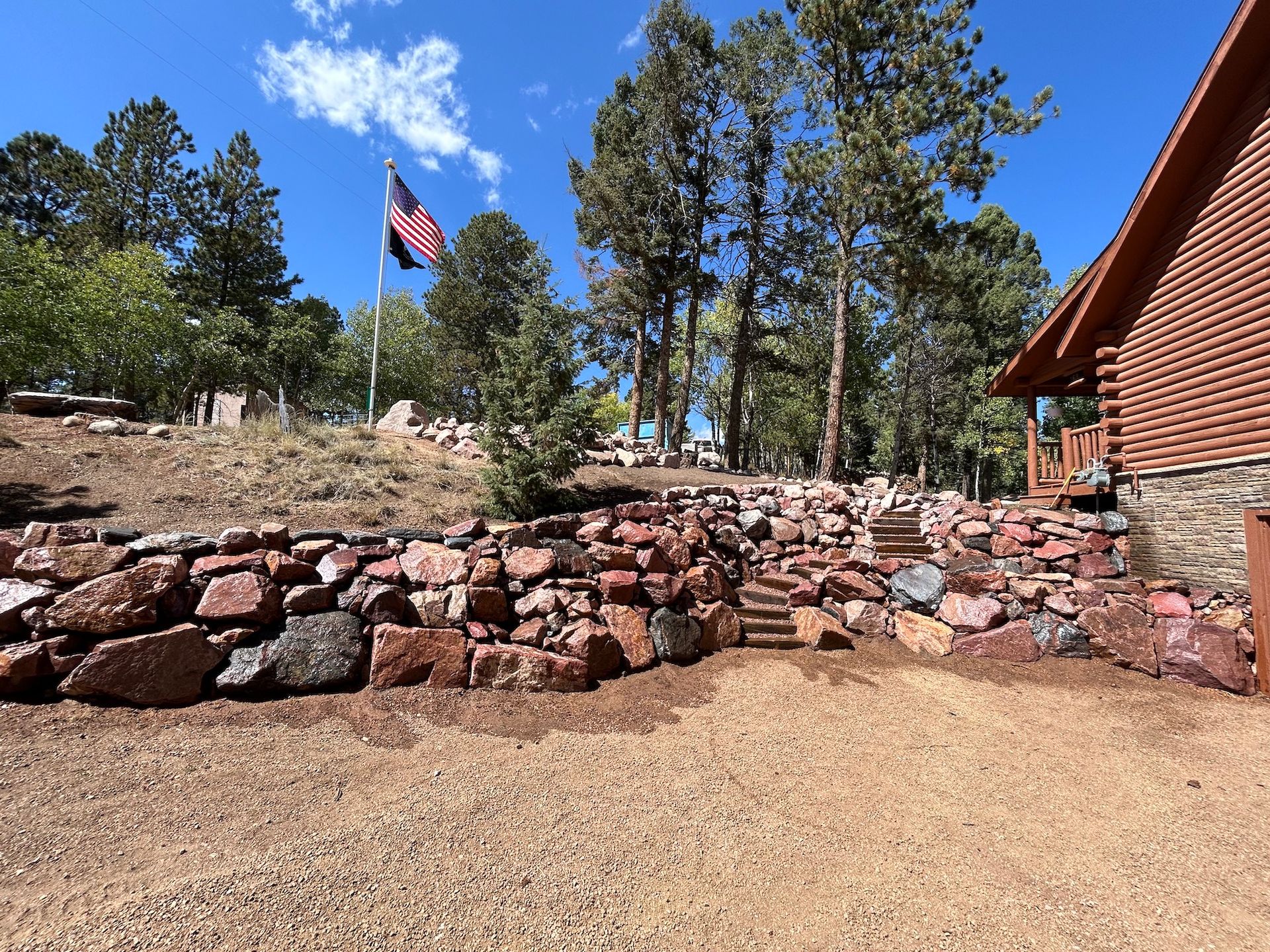 A large rock wall is in front of a house with a flag flying in the background.