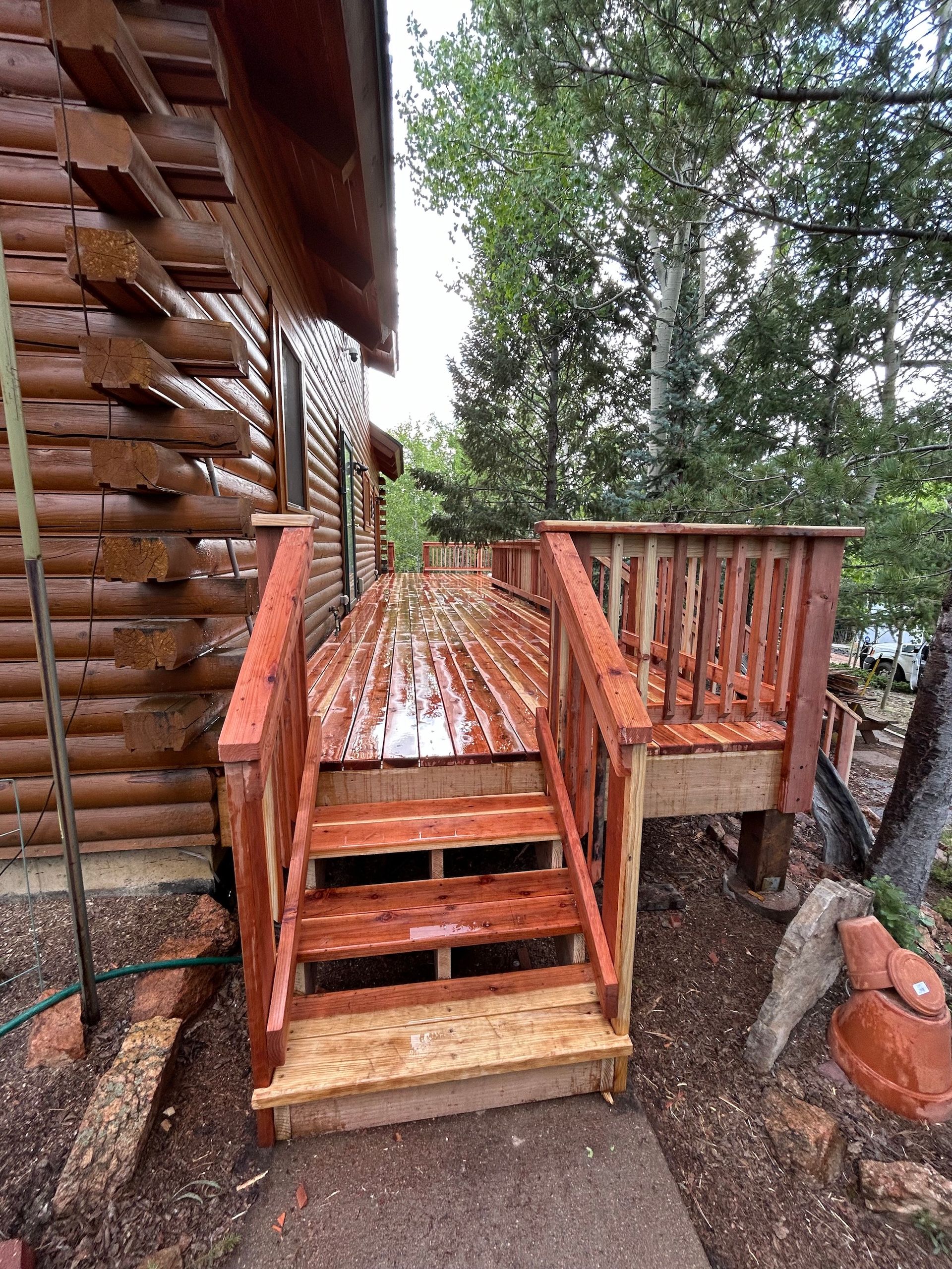 A wooden deck with stairs leading up to it next to a log cabin.