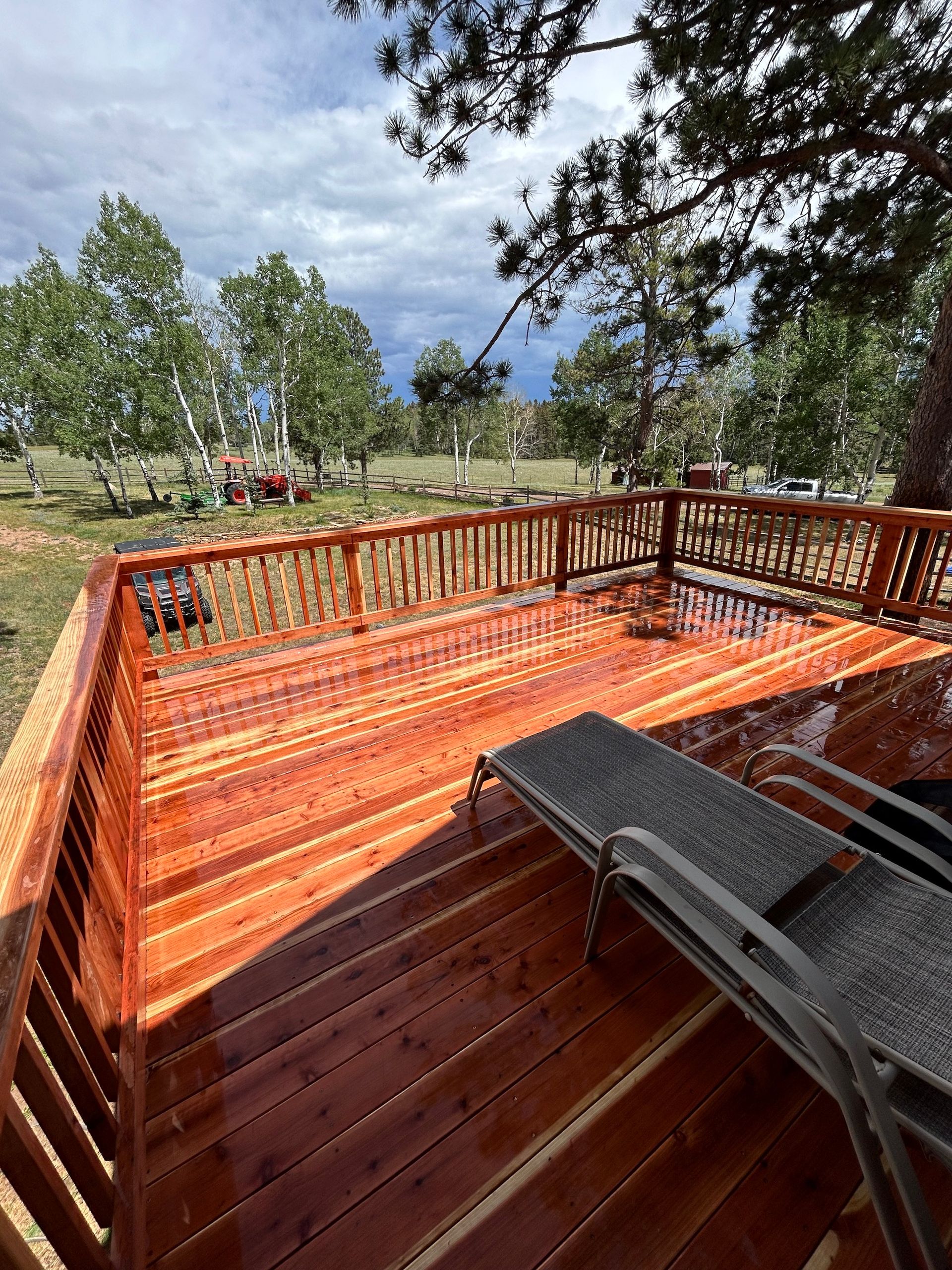 A wooden deck with a chair and a view of a field and trees.