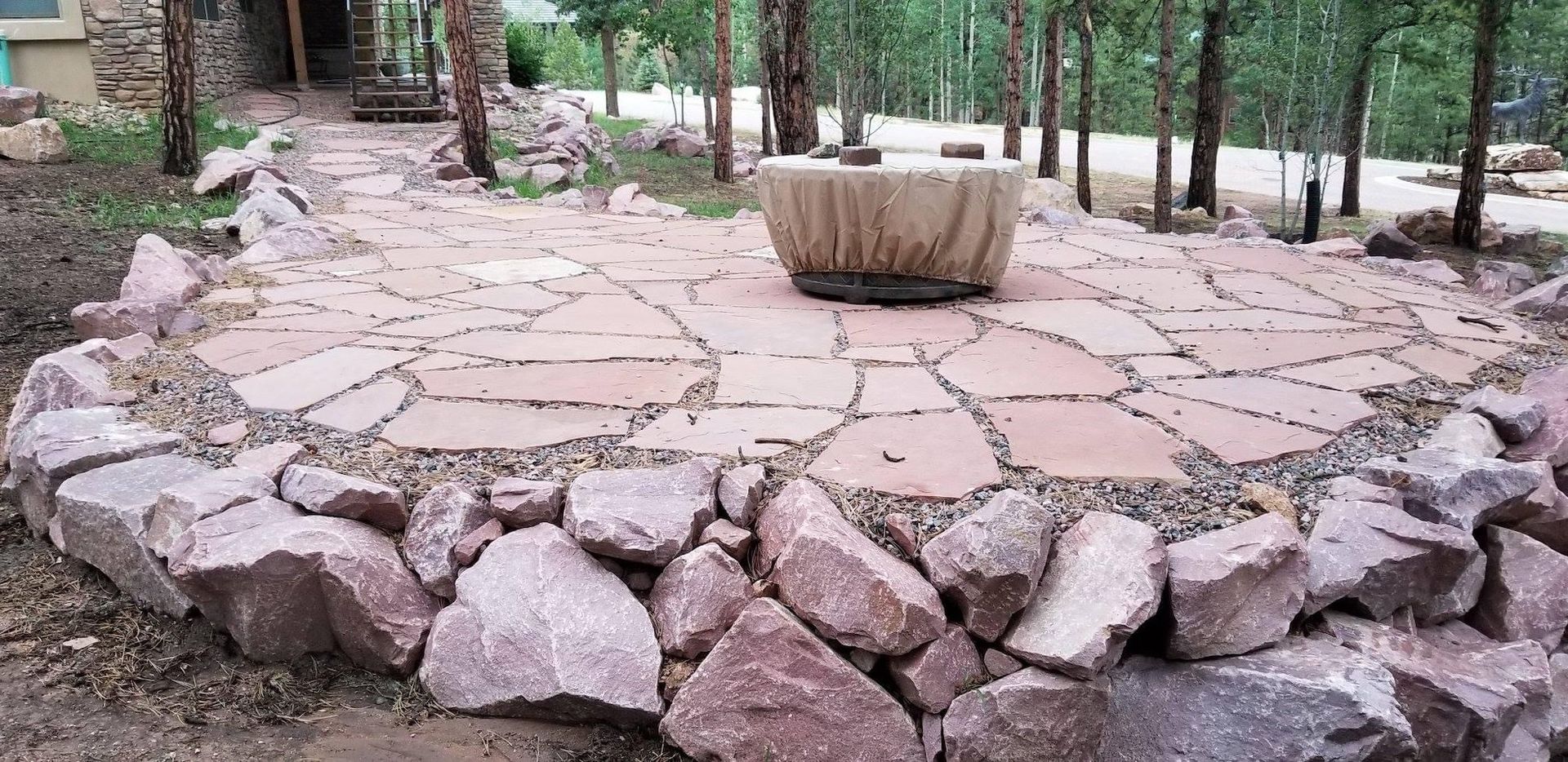 A stone patio with a fire pit in the middle of it surrounded by rocks.