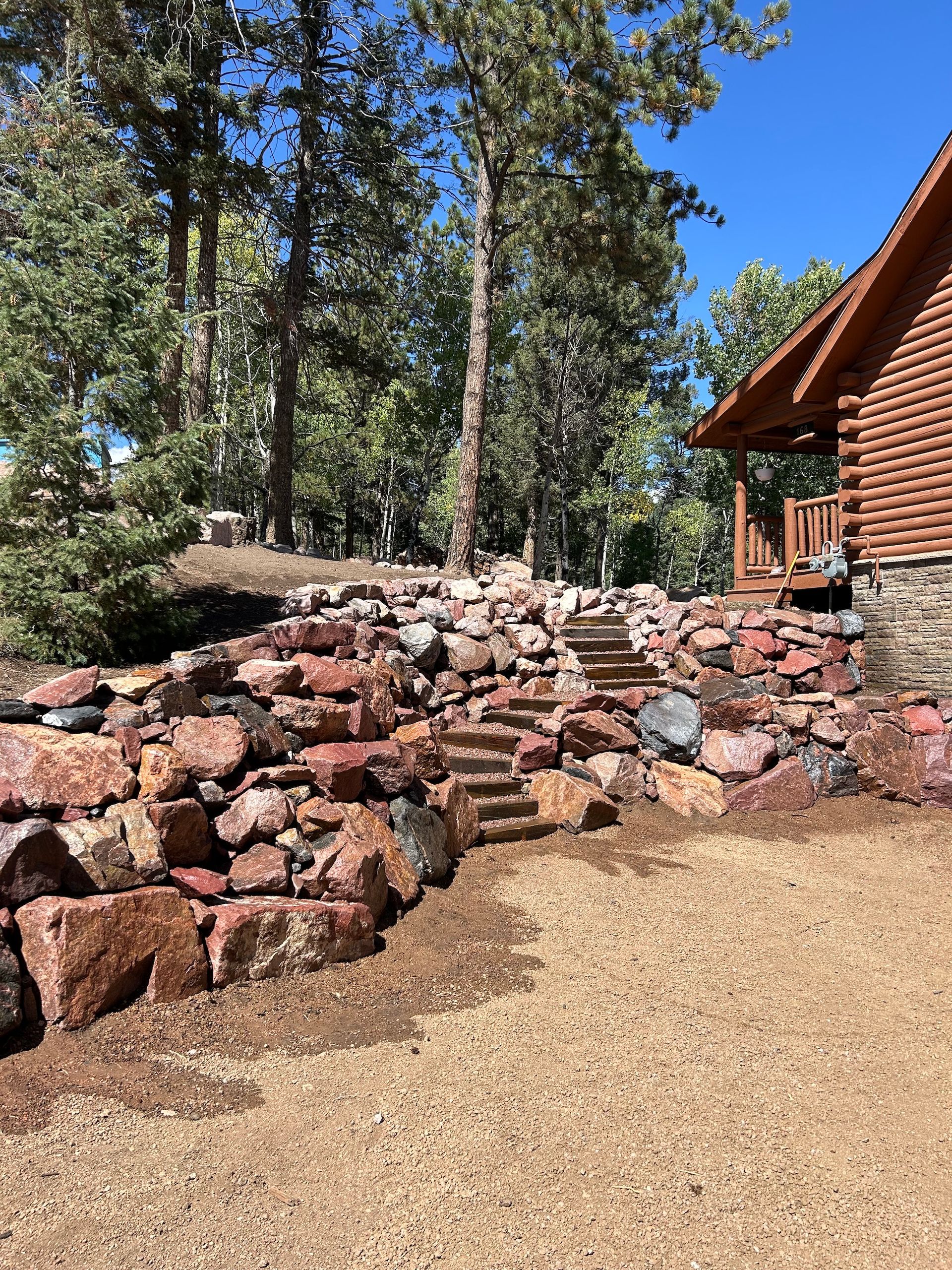 A log cabin with stairs leading up to it is surrounded by trees and rocks.