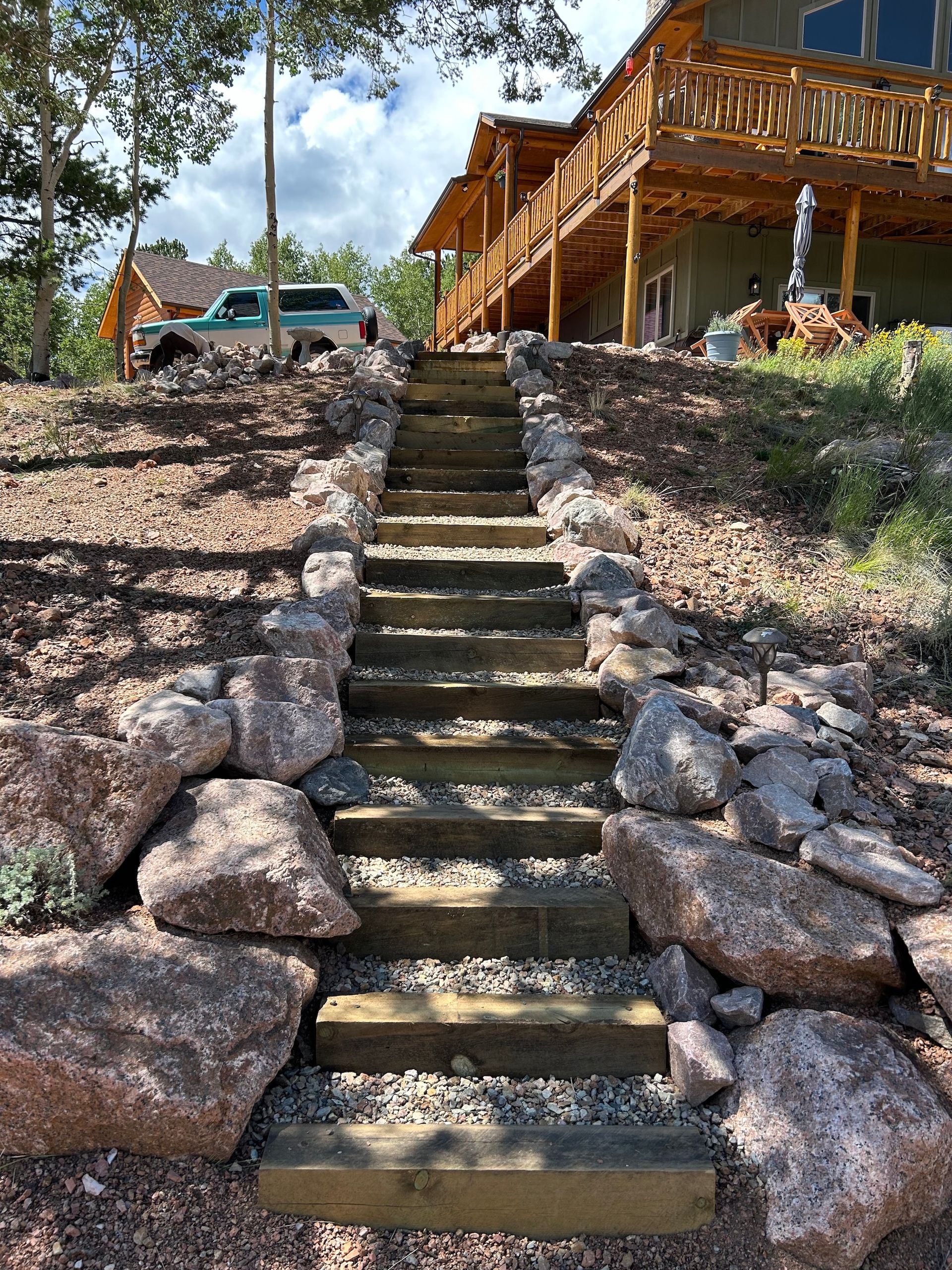 A set of wooden stairs leading up to a house surrounded by rocks.