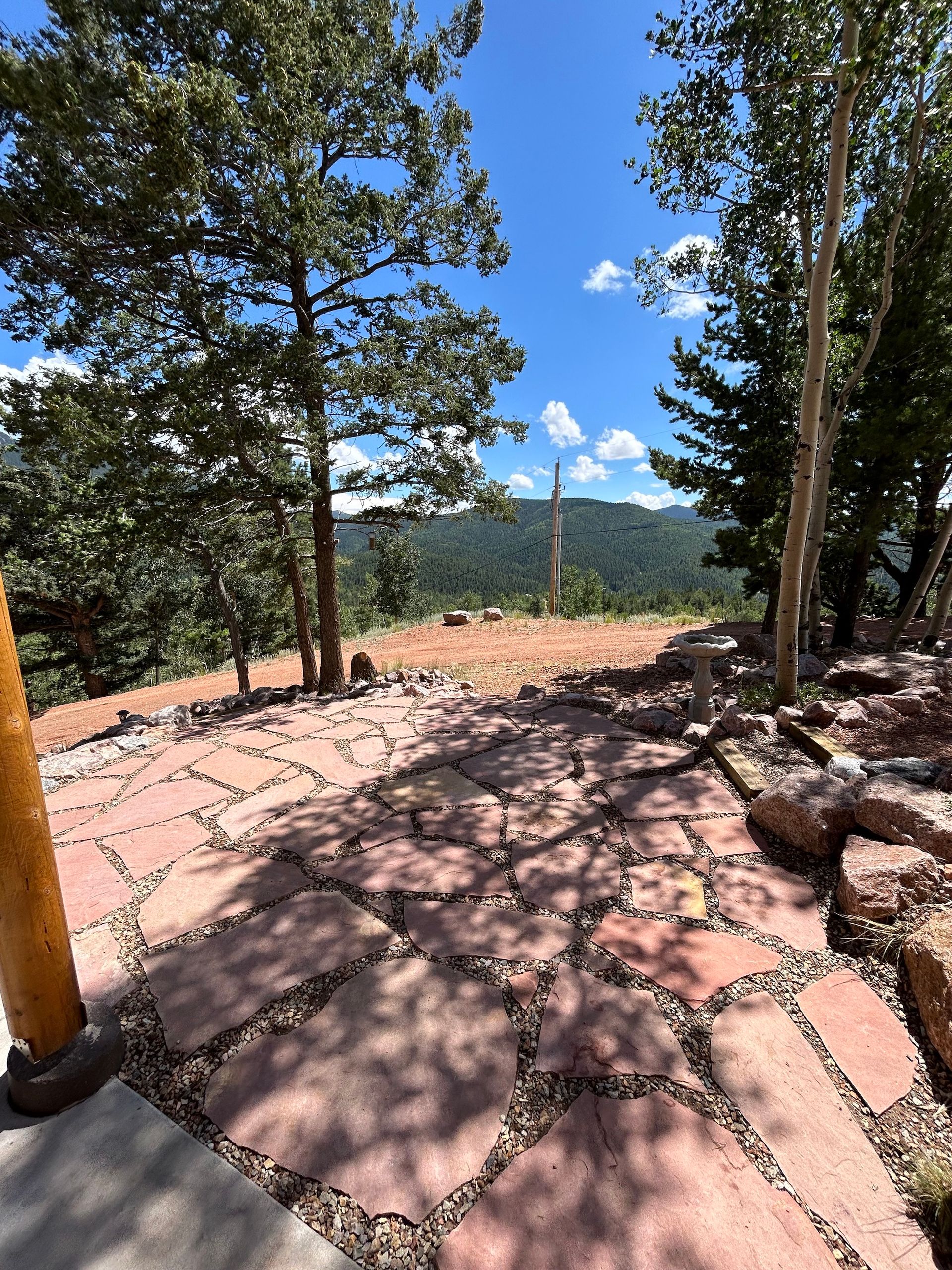 A stone walkway surrounded by trees and mountains on a sunny day