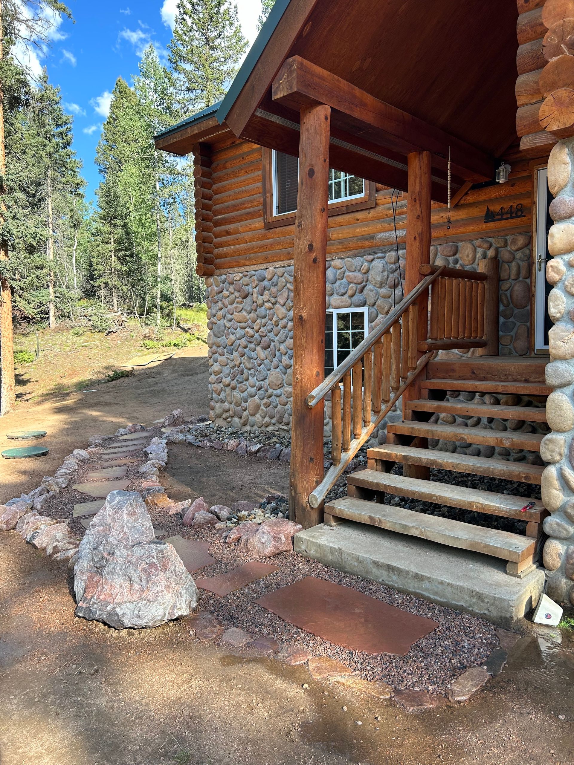A log cabin with stairs leading up to the porch and a stone wall.