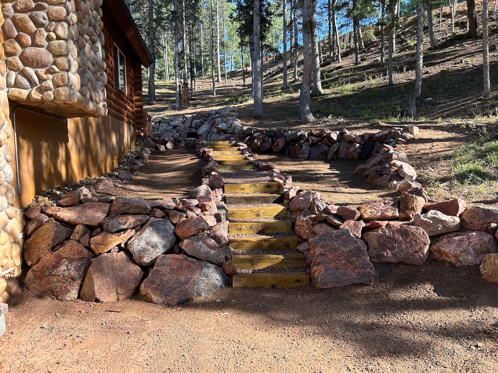 A stone wall with stairs leading up to a cabin in the woods.