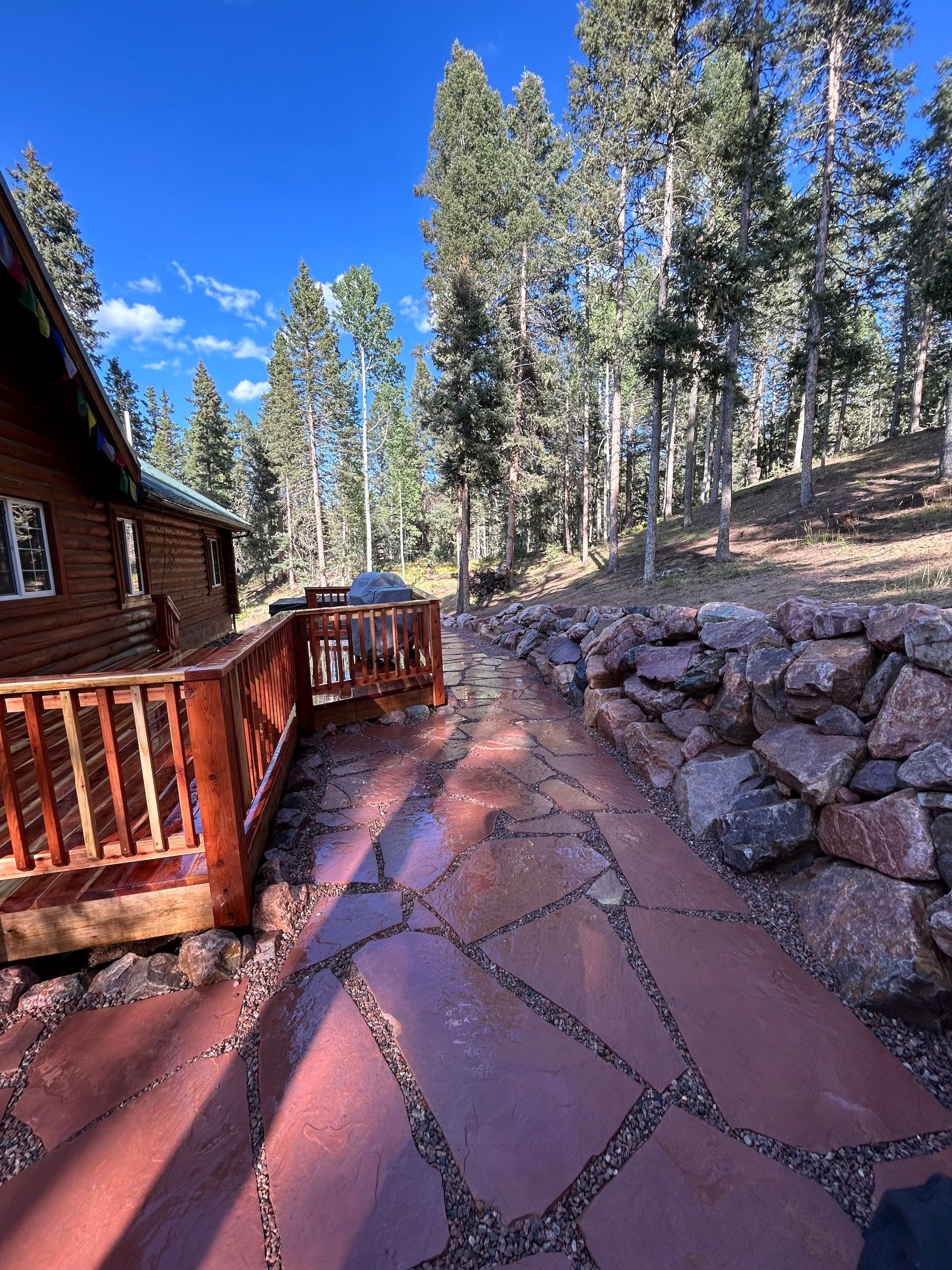 A wooden deck with a stone walkway leading to a cabin in the woods.