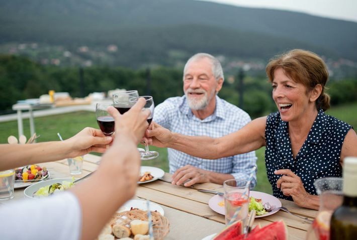 Friends toasting wine at an outdoor table with mountains in the background