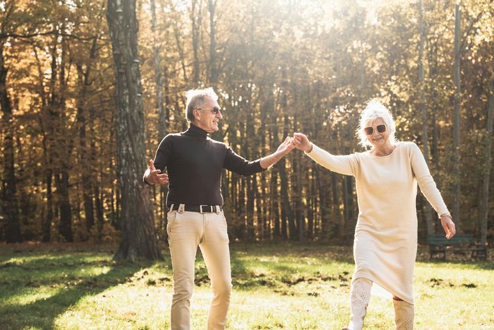 Two people holding hands in a sunlit forest clearing, with golden autumn trees in the background.