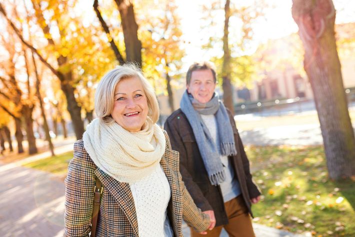 Two people smiling on a sunny autumn path with yellow leaves and trees