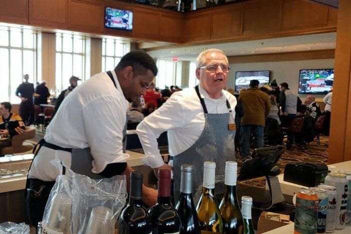 Two men serving wine at a tasting booth in a busy indoor hall