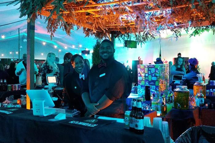 People at a neon-lit bar with drinks, shelves, and tropical decor under blue lighting