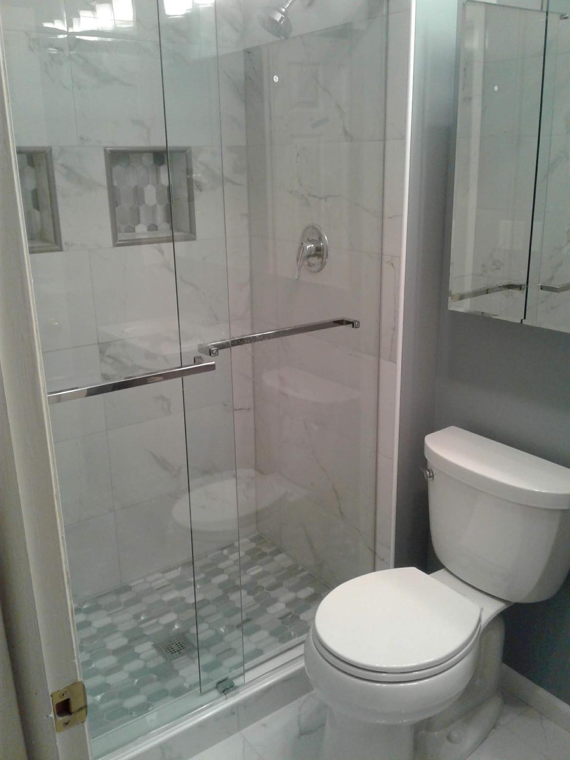 Standing shower stall remodeling with glass shower doors, pattern floor and wall tiling, new toilet, and granite quartz tiling floors.