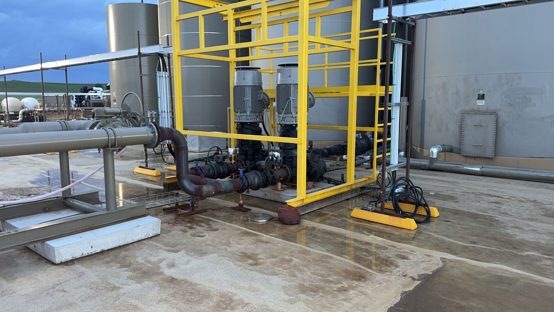 Industrial equipment with yellow safety railings, pipes, and valves in a wet concrete utility area