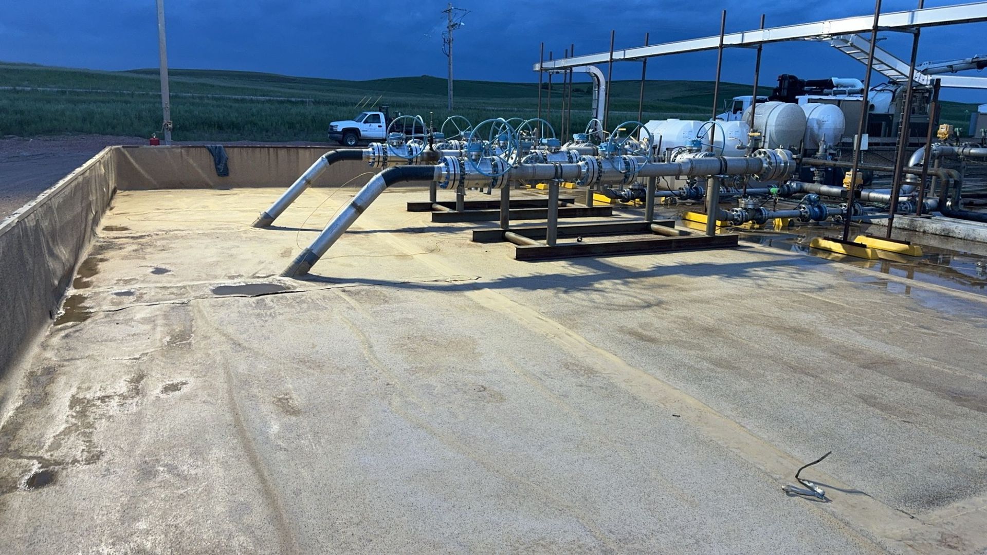 Industrial rooftop equipment with pipes and tanks beside a concrete parapet, overlooking the ocean