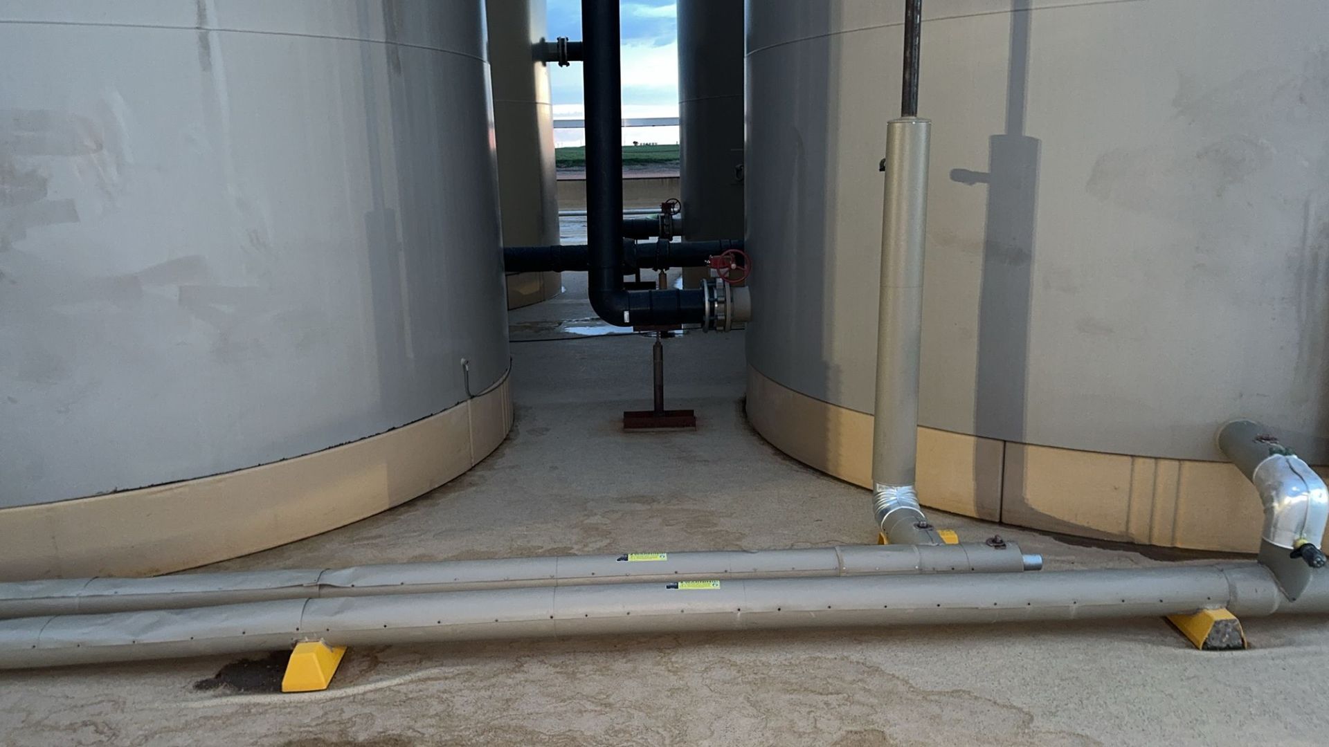 Two large gray tanks with pipes and a small utility cart in an industrial area.