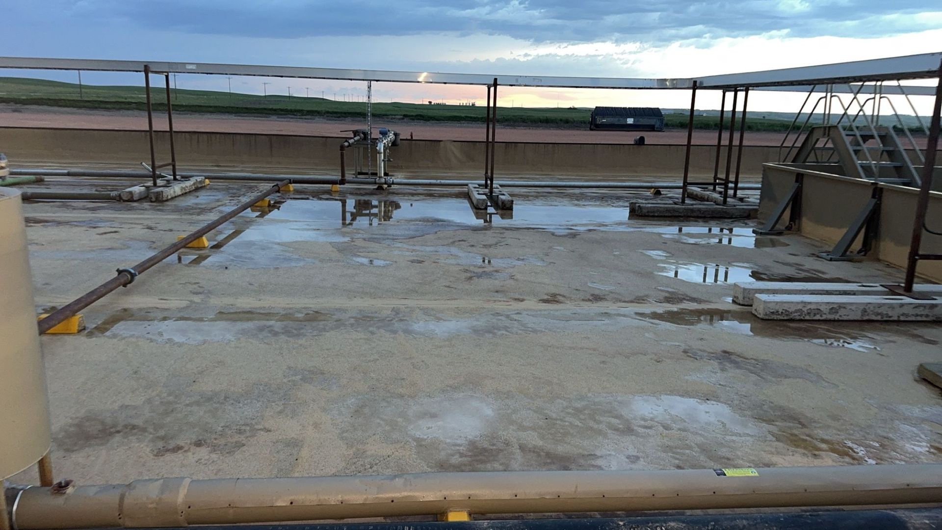 Wet rooftop with metal rails, puddles, and a cloudy sky in the distance