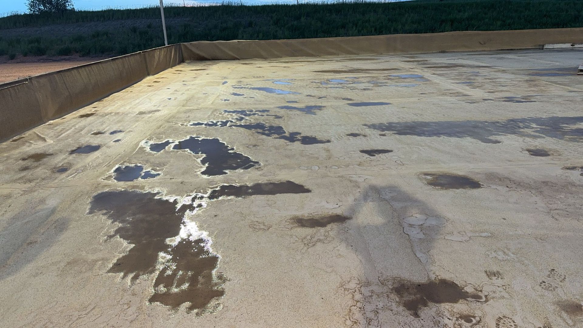 Large concrete lot with puddles and dark stains beside a low wall under a clear sky