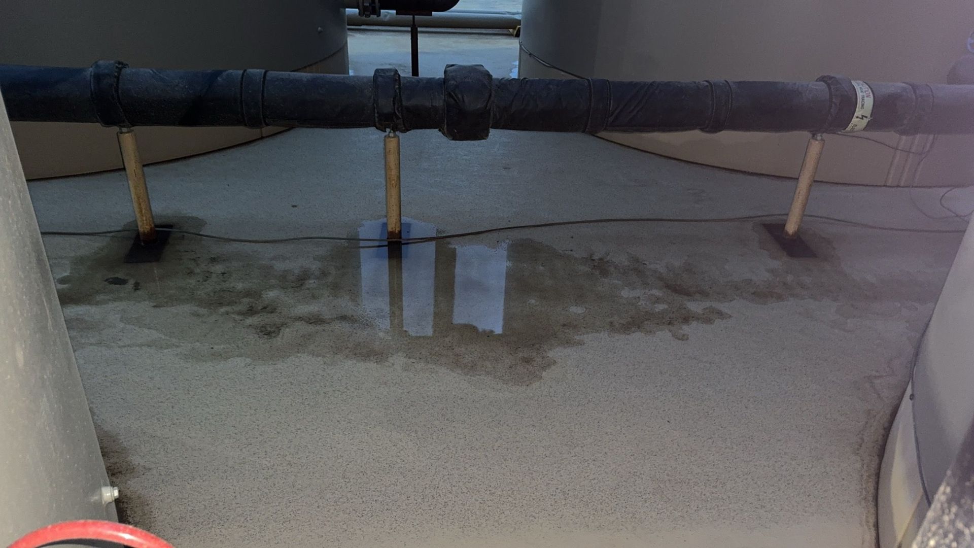 Rusty pipes and small supports over a damp concrete floor in an industrial area