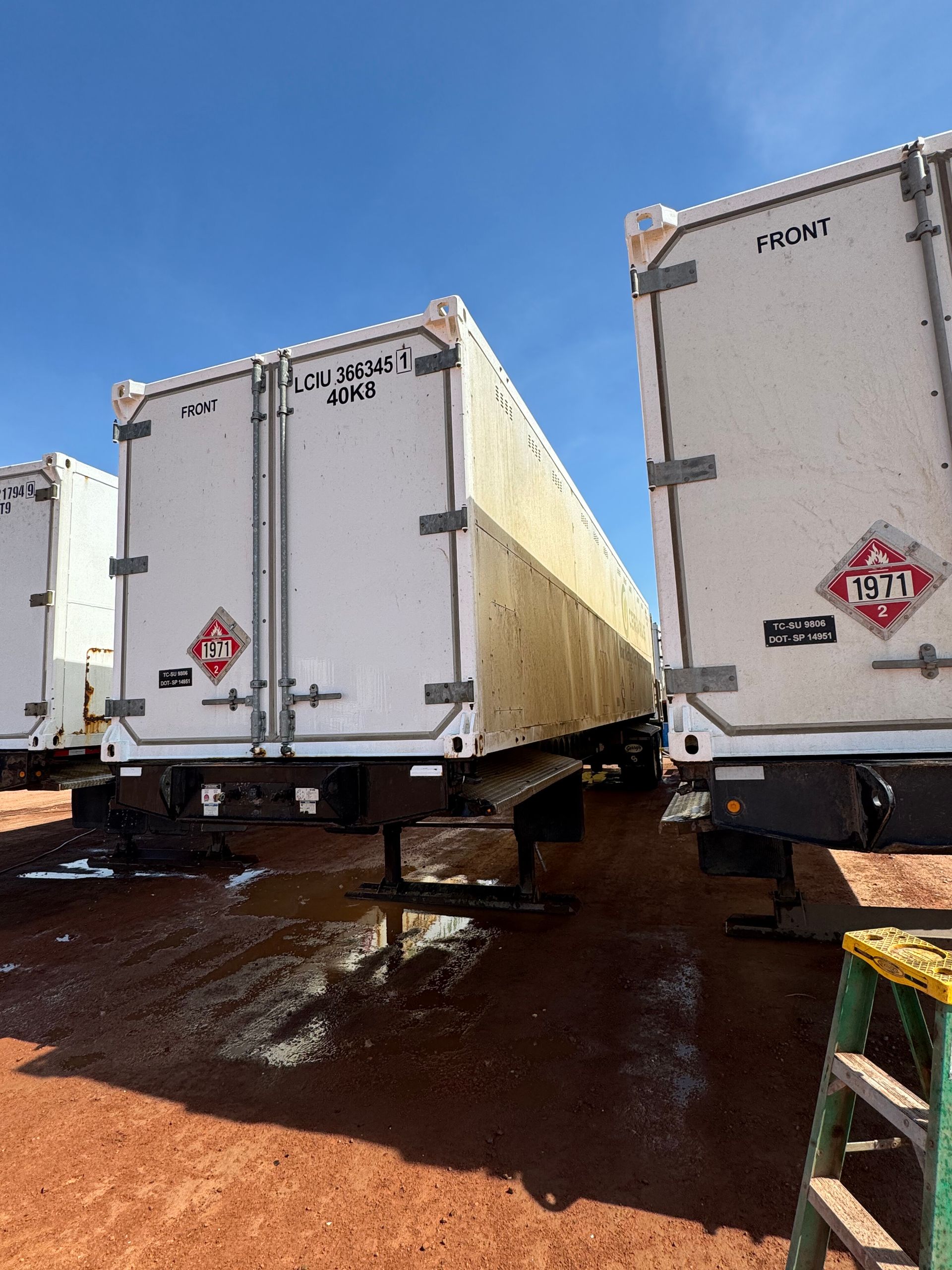 Two white refrigerated trailers on a muddy lot under a blue sky
