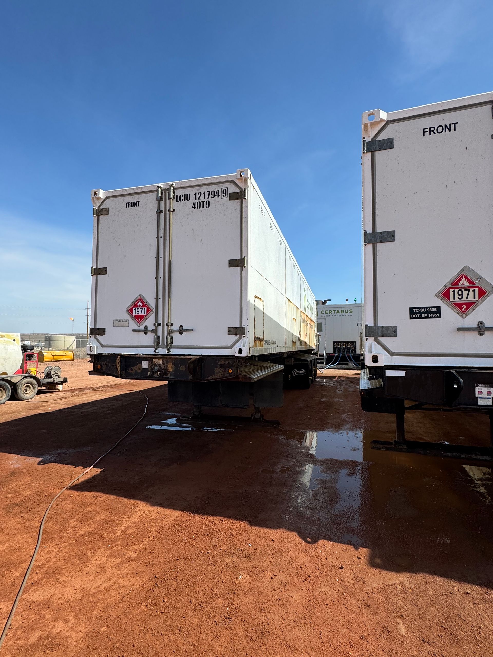 Two white semi-trailers parked on muddy red ground under a blue sky