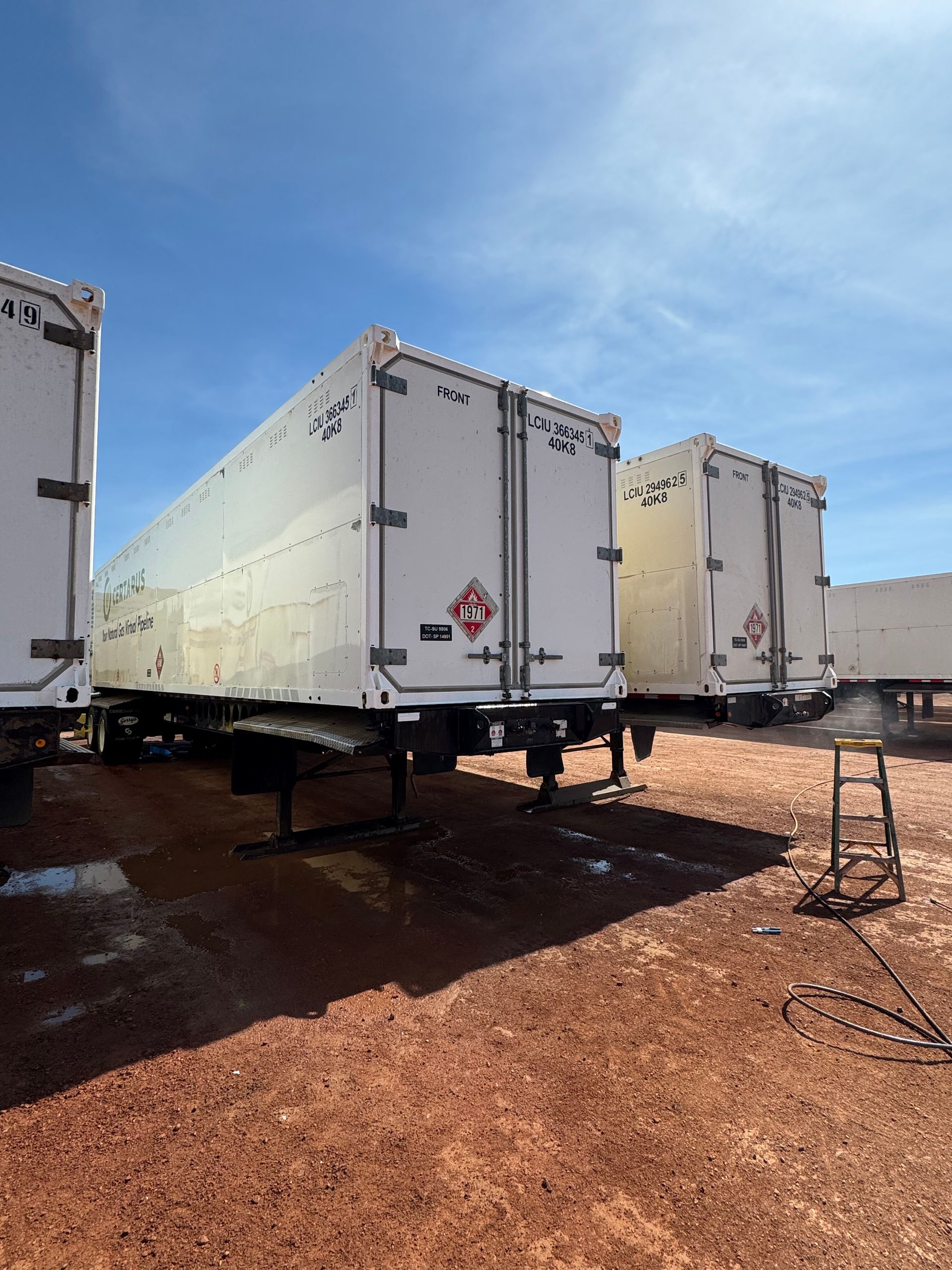 White semi-trailers parked on a reddish gravel lot under a bright blue sky.