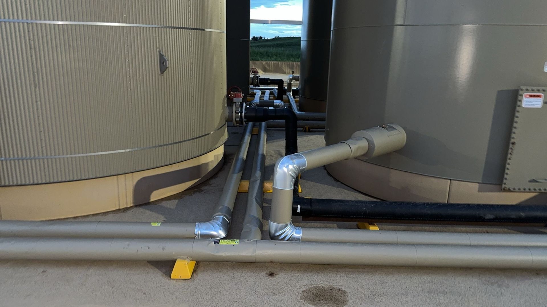 Industrial tanks with gray pipes and hoses in a narrow maintenance area outdoors