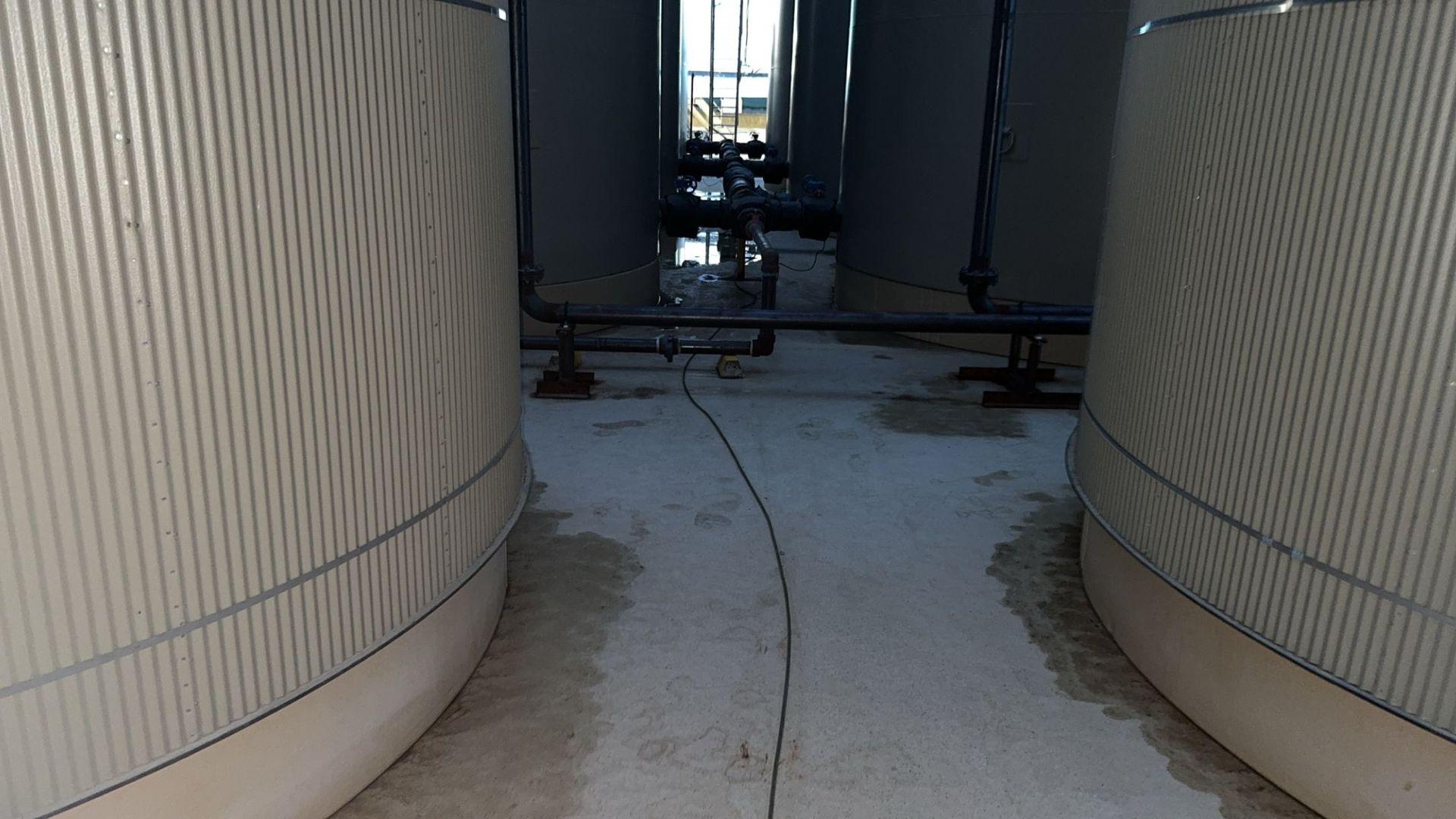 Narrow walkway between large white curved tanks, with a dark pipe crossing in the distance.