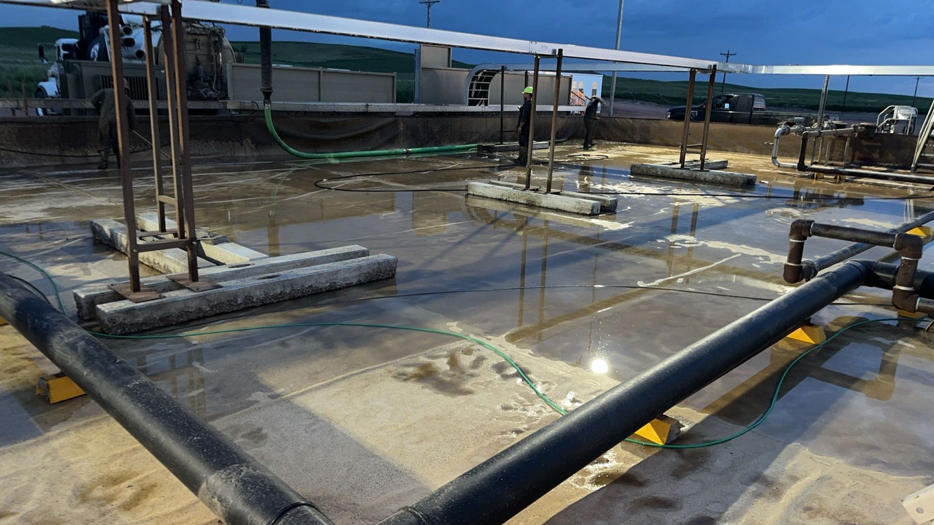 Wet concrete rooftop with black pipes and metal supports under a blue sky