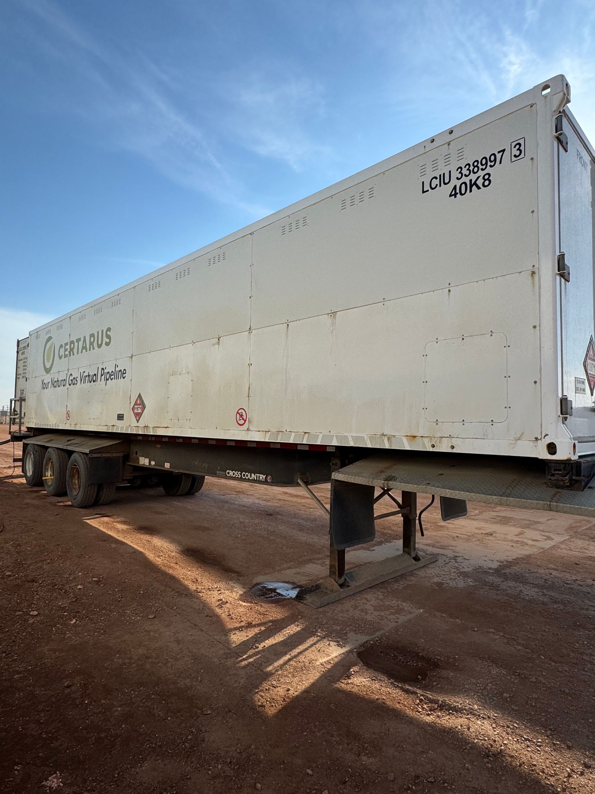 White utility trailer on jack stands in a dirt lot under a blue sky
