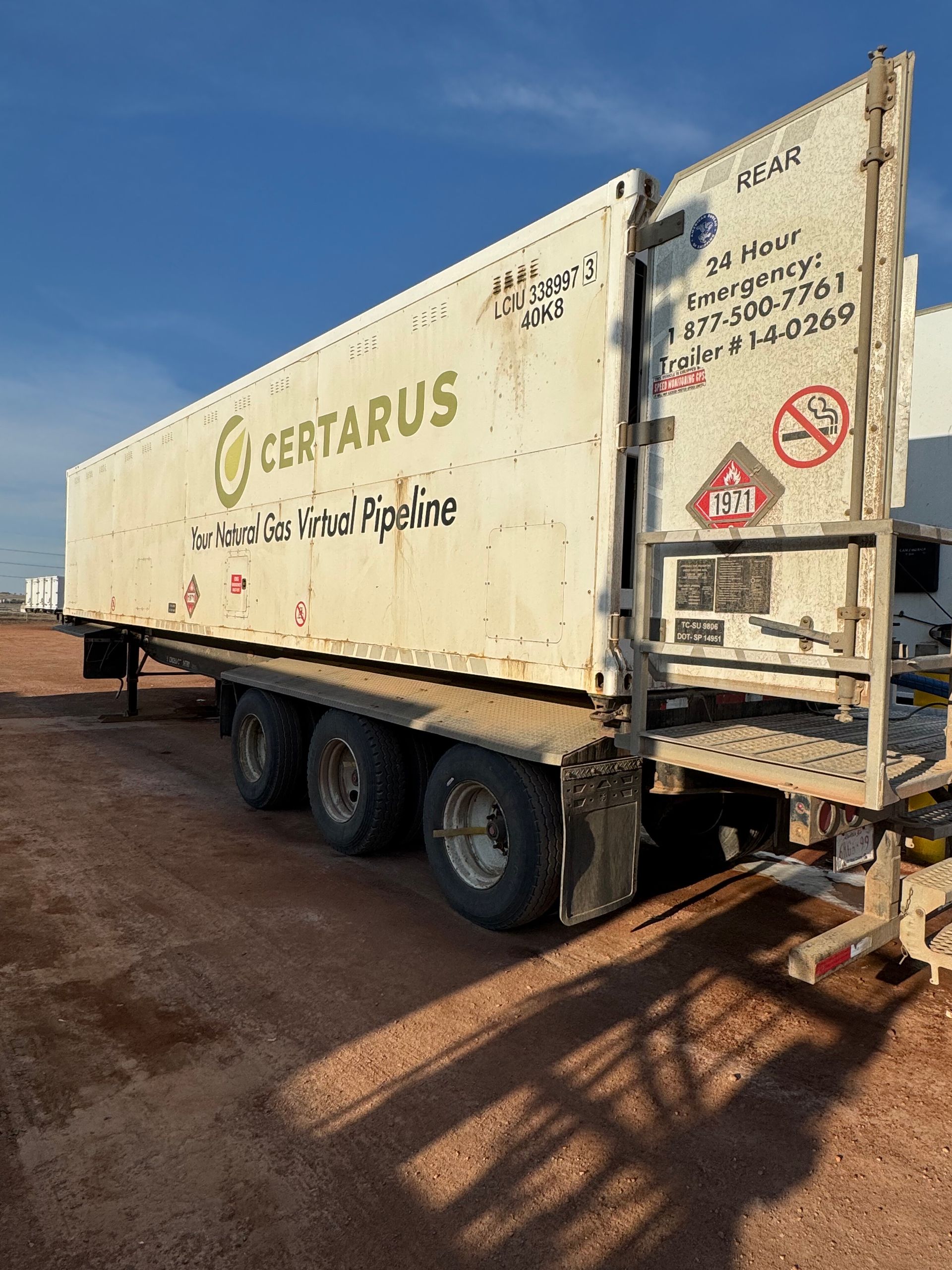 White Certarus tanker trailer parked on a dirt lot under a blue sky, side view with hazard markings.