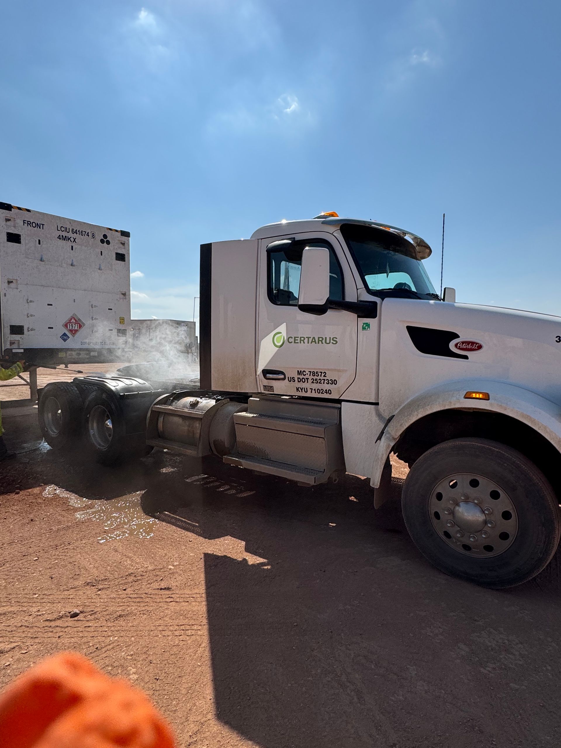 White work truck parked beside a building on a dirt lot under a bright blue sky.
