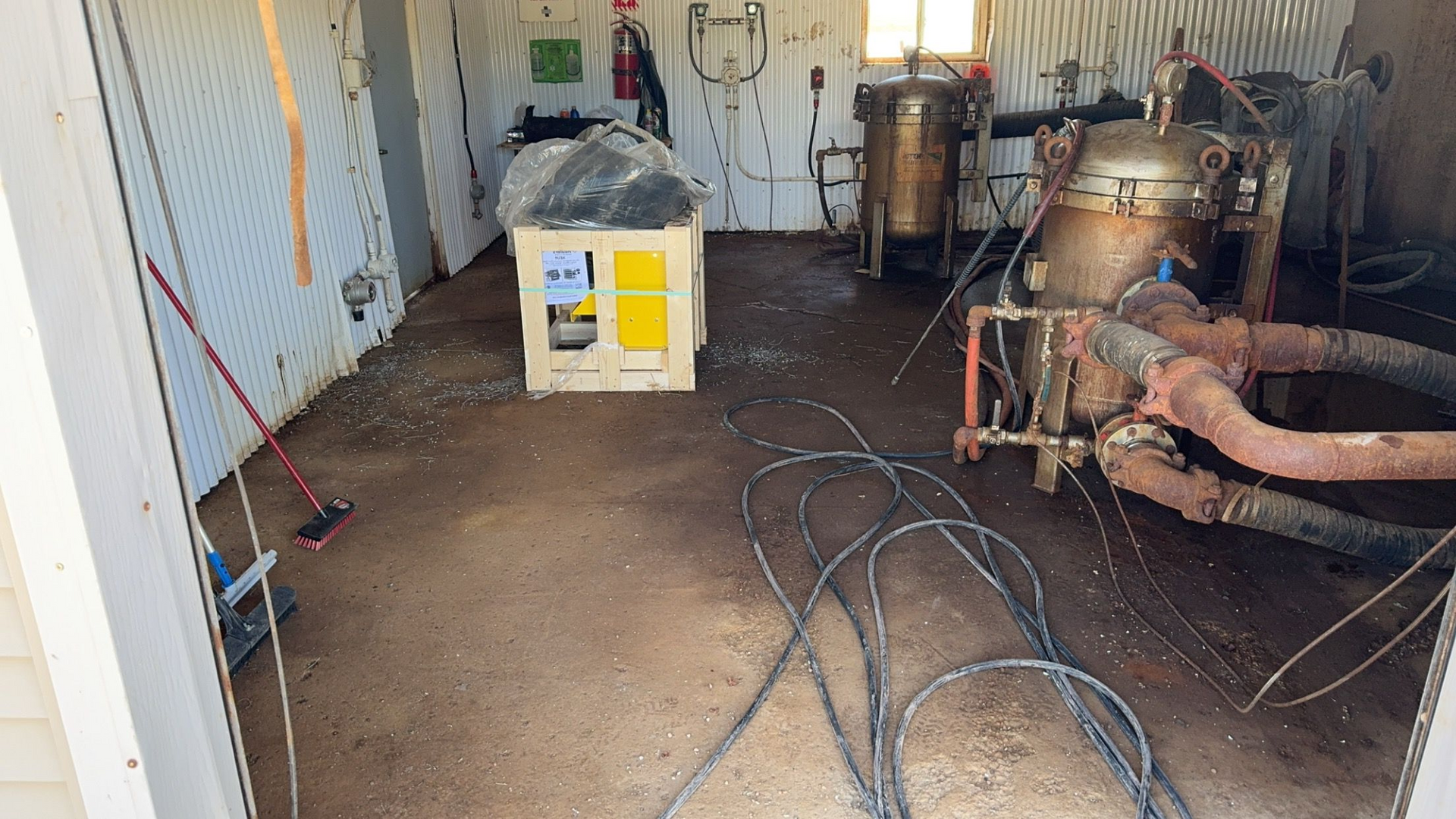 Cluttered workshop with a white-and-yellow machine, tangled cables, and large metal equipment on the right.