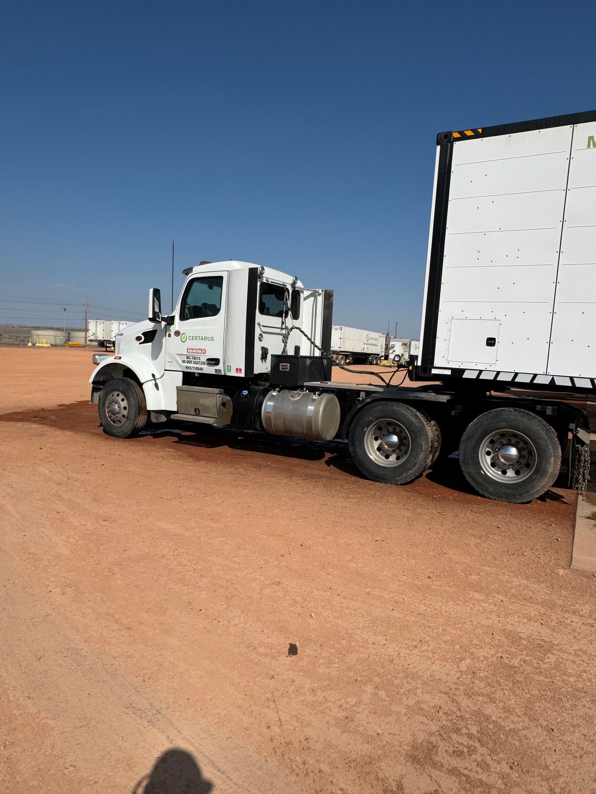 White semi-truck with trailer parked on a red dirt road under a clear blue sky.