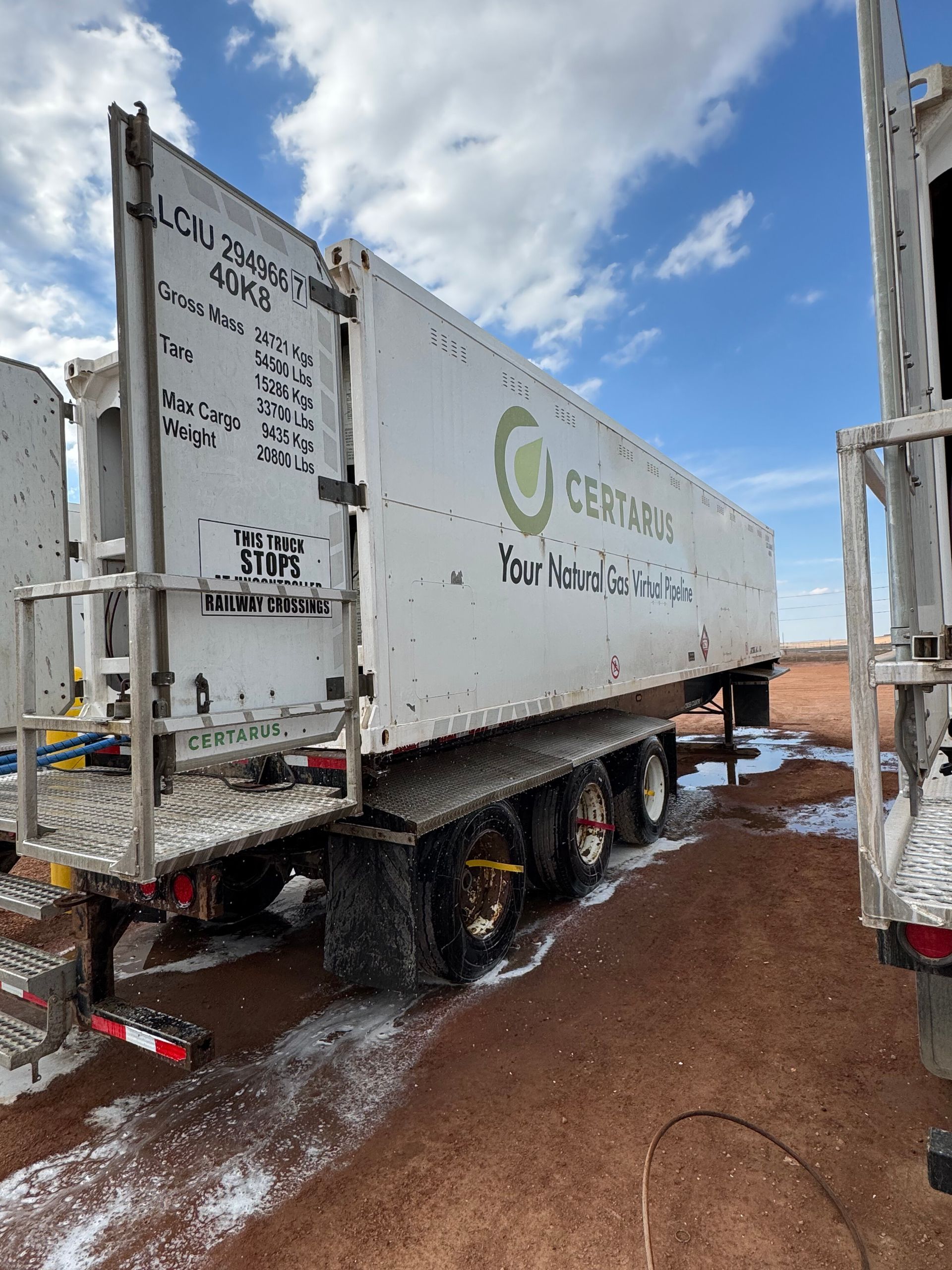White truck with green logo on muddy road beside another truck under a cloudy sky