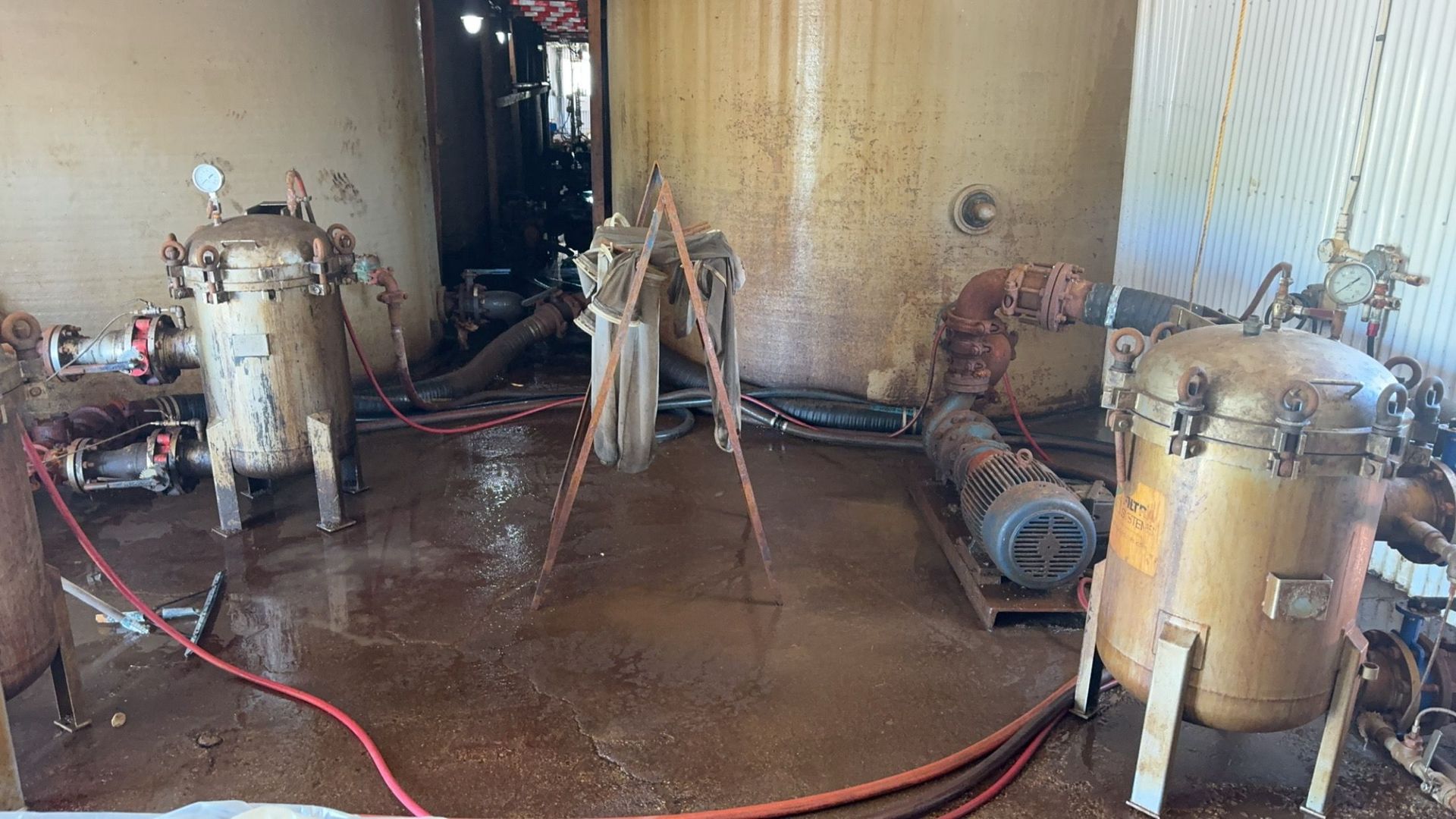 Industrial room with pipes, tanks, and hoses on a wet floor during cleanup or maintenance