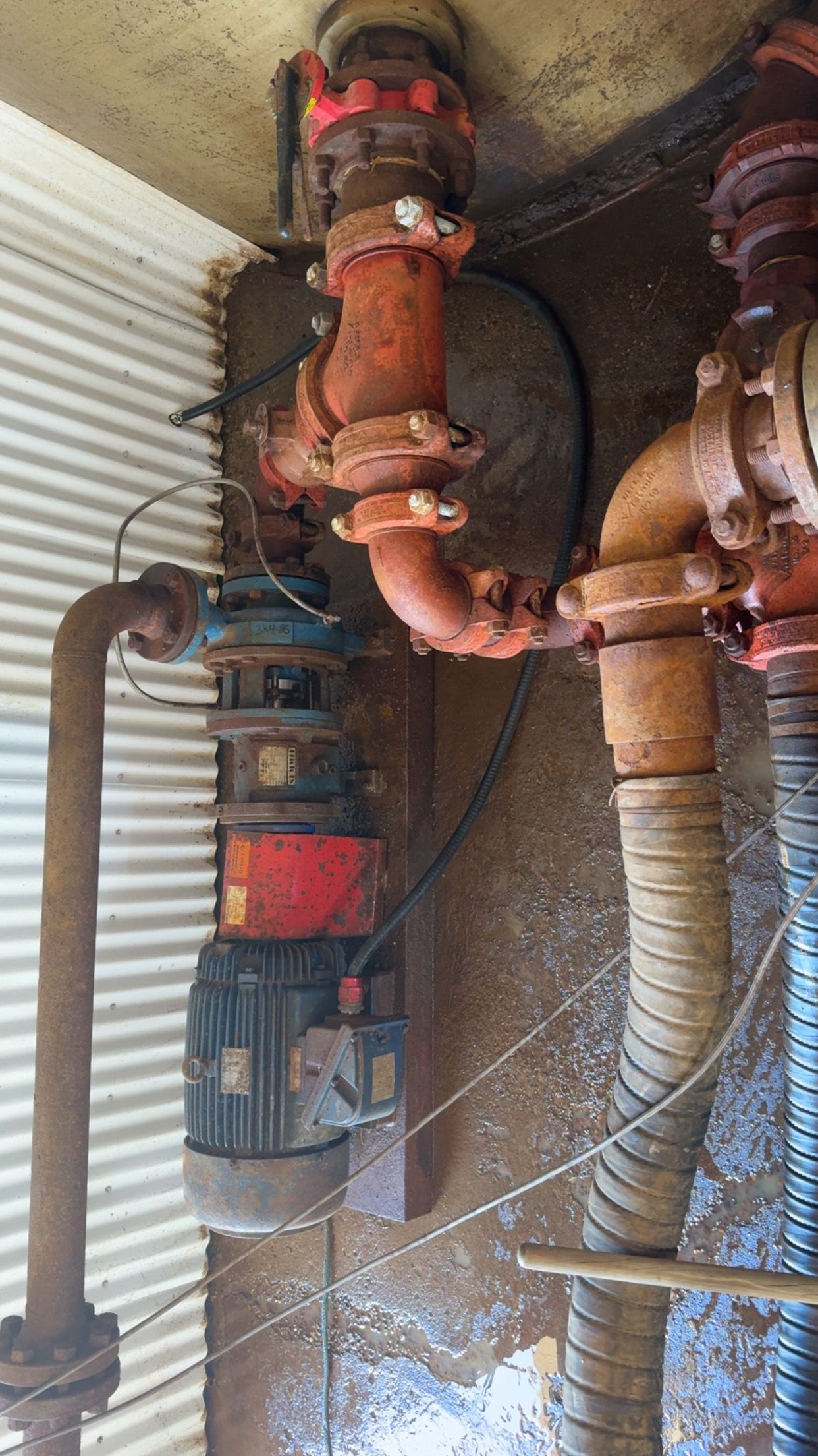 Rusty industrial pipes and valves with a red motor pump in a cramped utility area