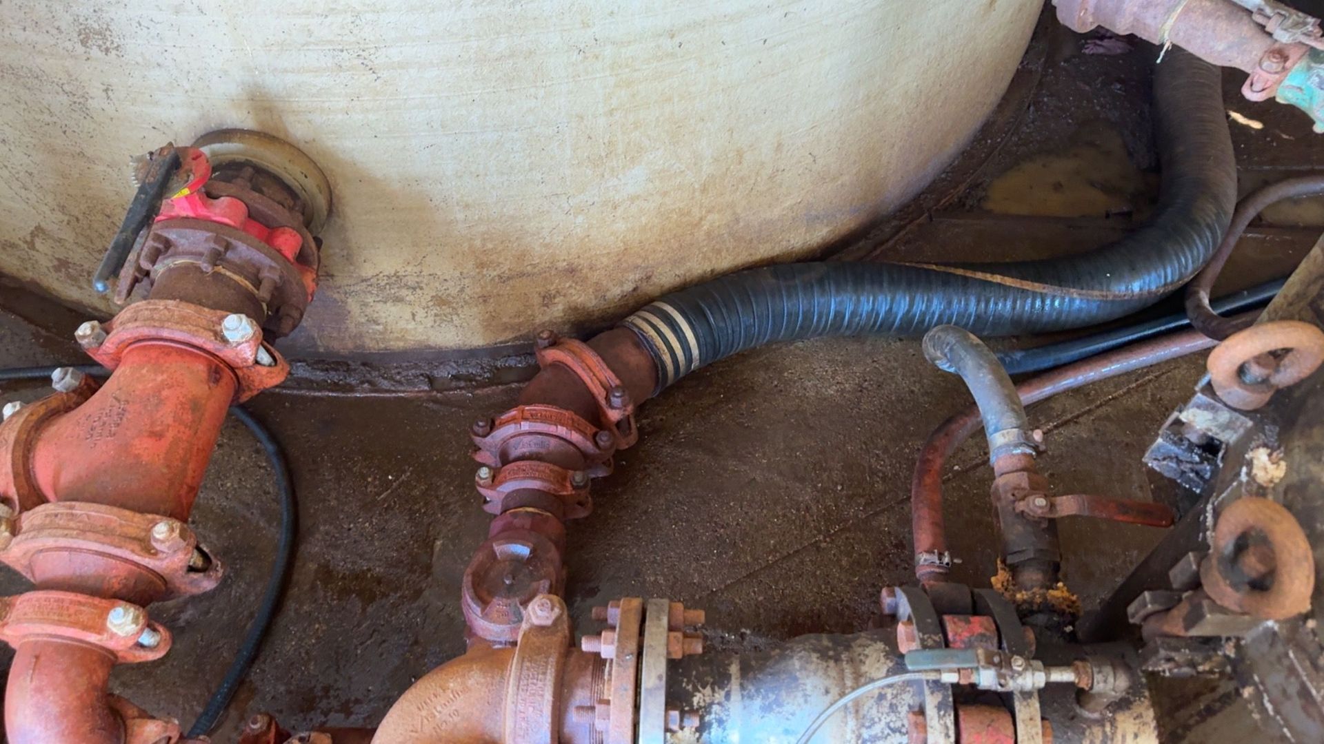 Rusty pipes and valves connected to a large tank in an industrial setting.