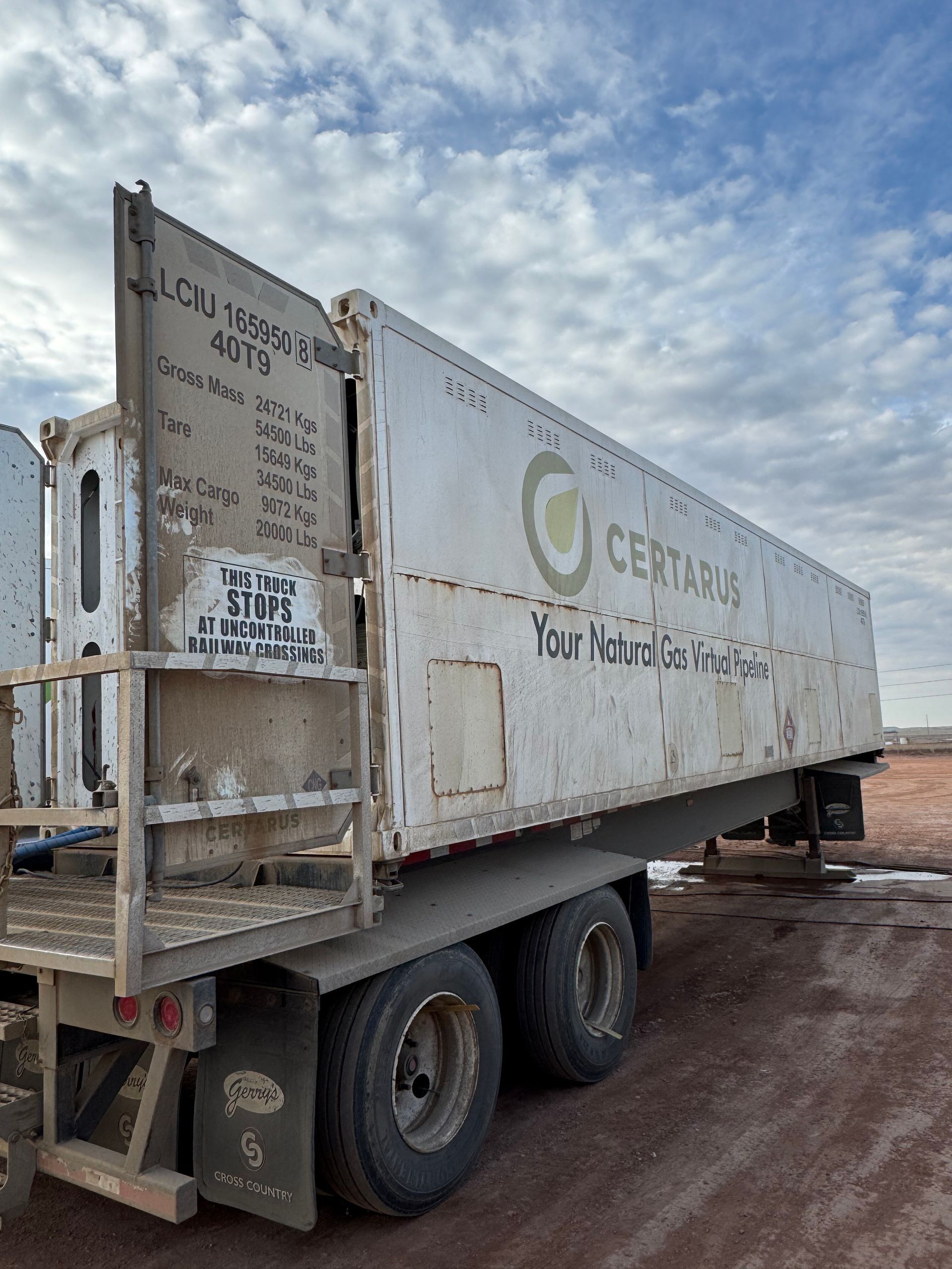 Weathered white utility trailer on a muddy lot under a cloudy sky