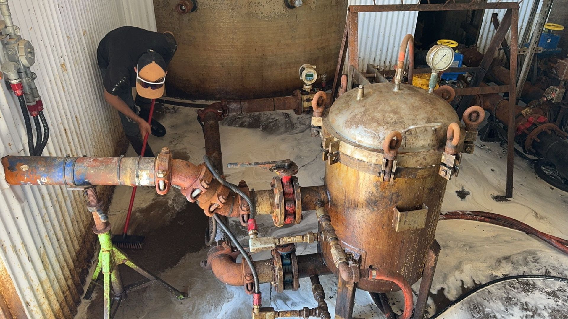 Rusty industrial machinery and pipes in a cluttered workshop area.