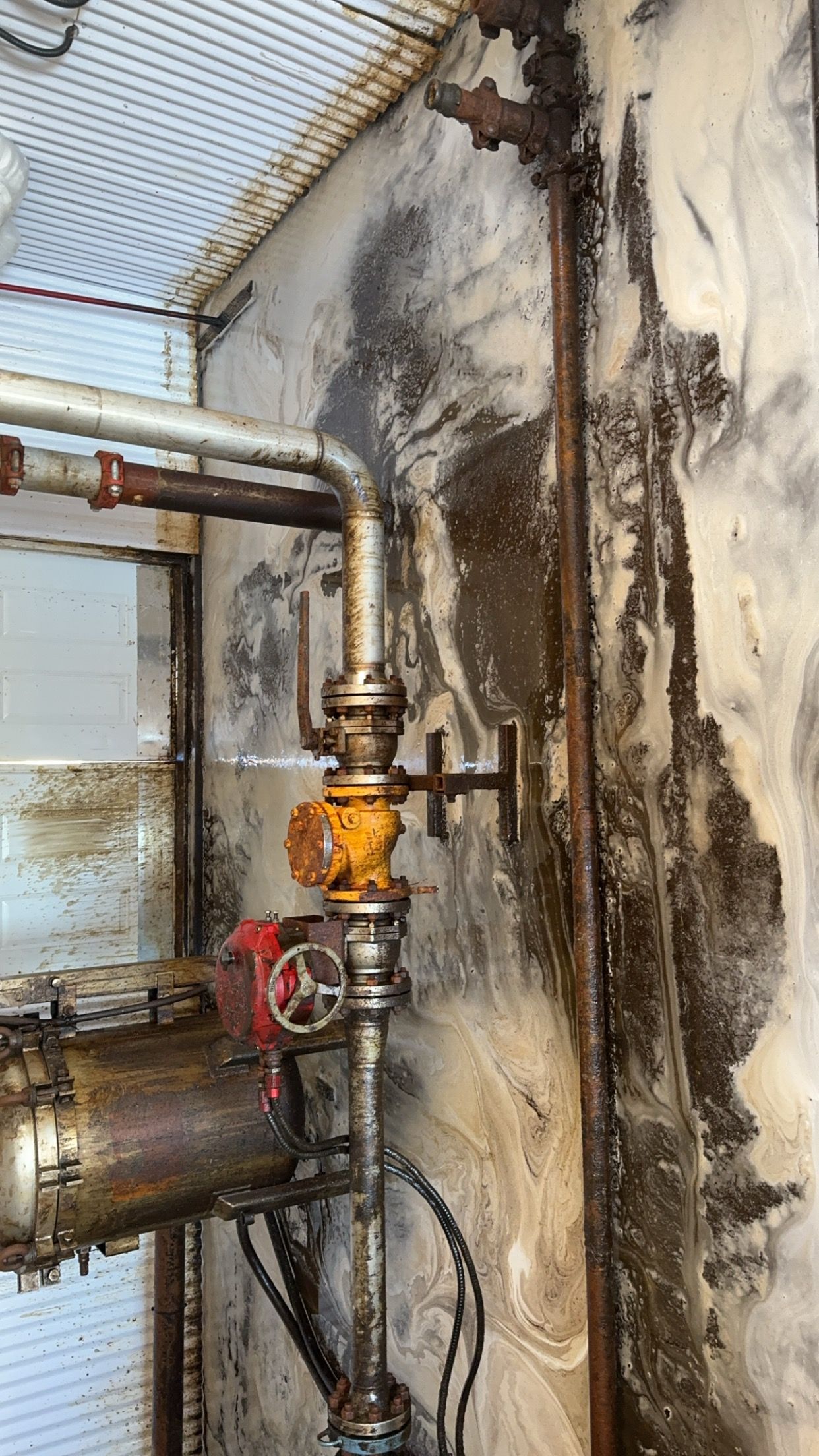 Industrial pipes and valve on a wall with heavy water damage and black mold stains