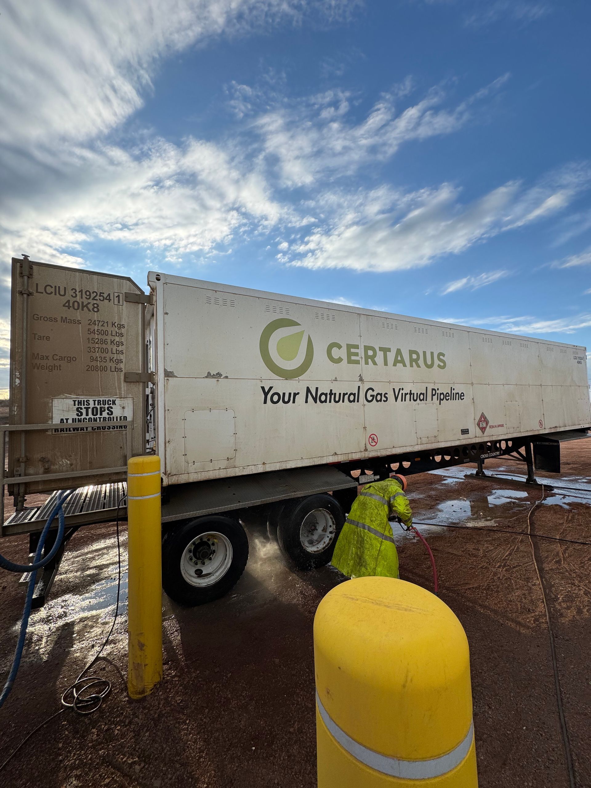 White Certarus trailer parked on wet ground under a cloudy sky, with yellow bollards in front.