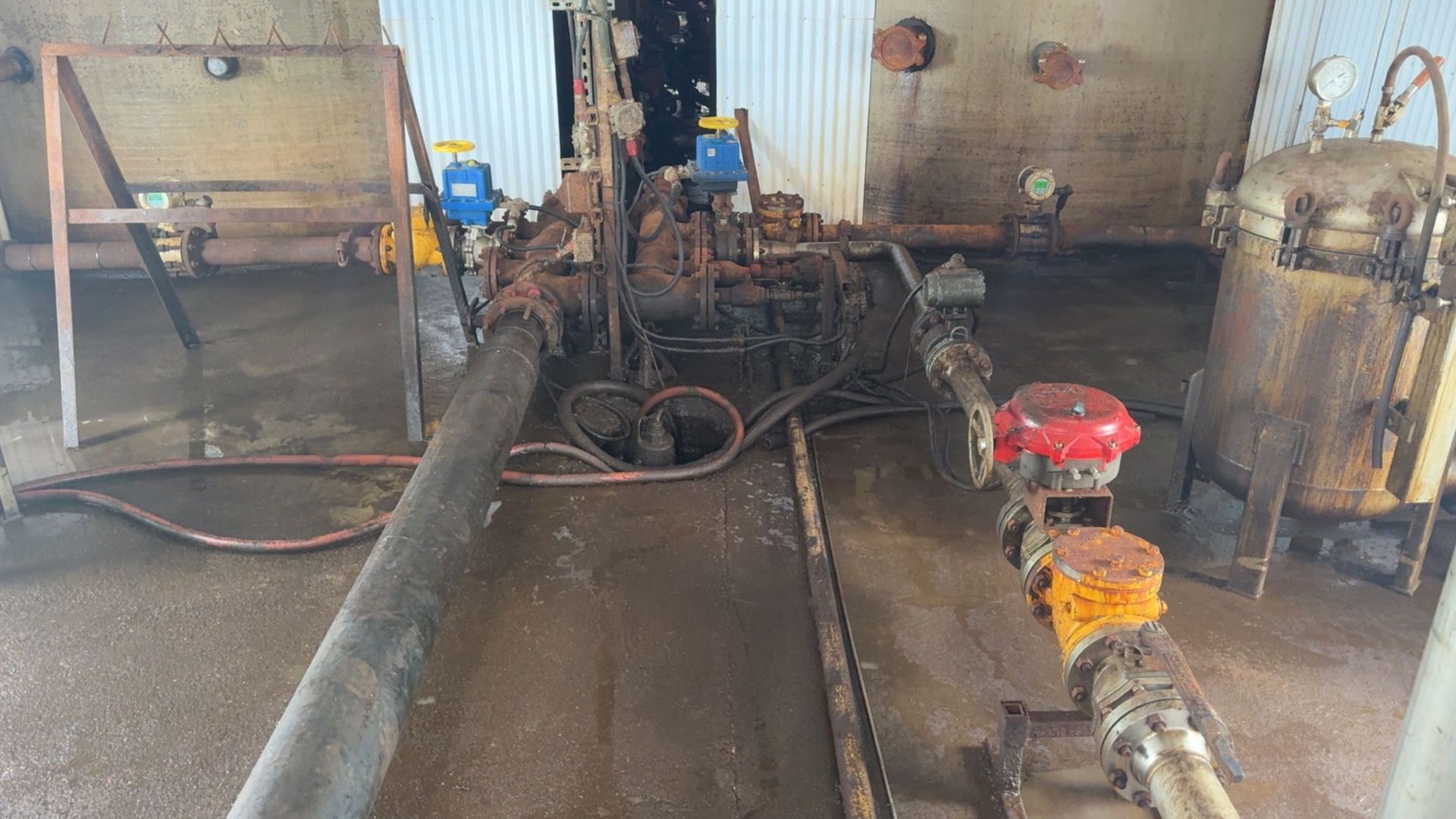 Industrial pump room with hoses and machinery on a wet floor, including a red motorized pump in front.