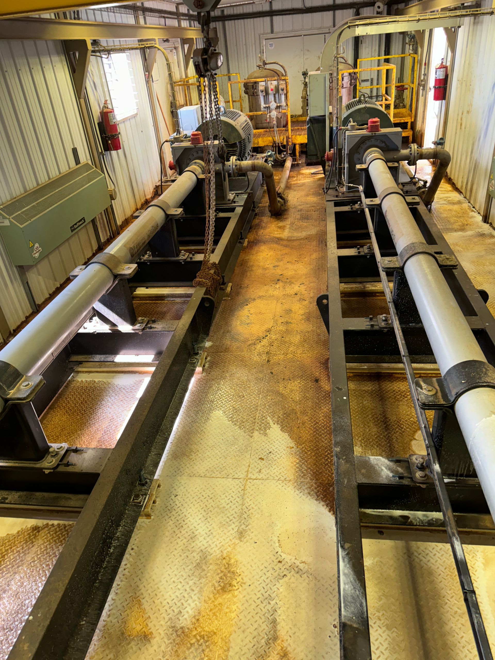 Industrial engine room with pipes, metal equipment, and a narrow central walkway.
